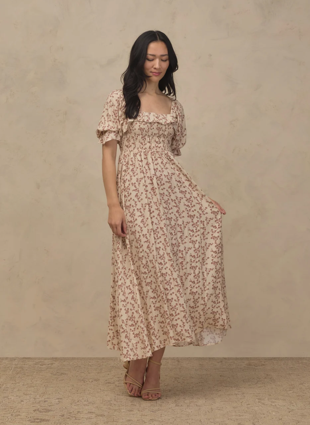 Woman wearing a floral smocked midi dress with puff sleeves in a cream and brown print.