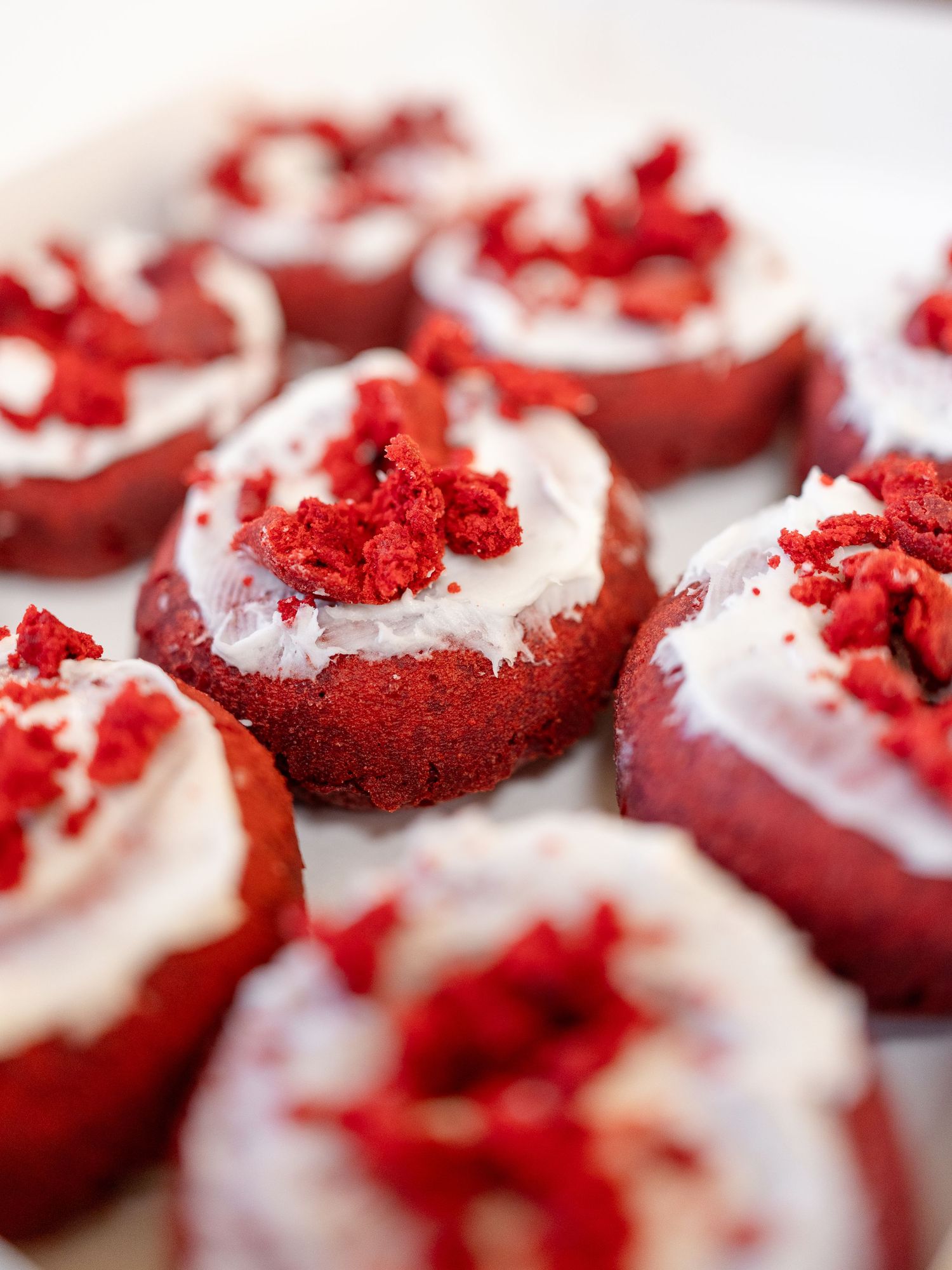 Close-up view of red velvet cake bites topped with white cream cheese frosting and red velvet crumbs.