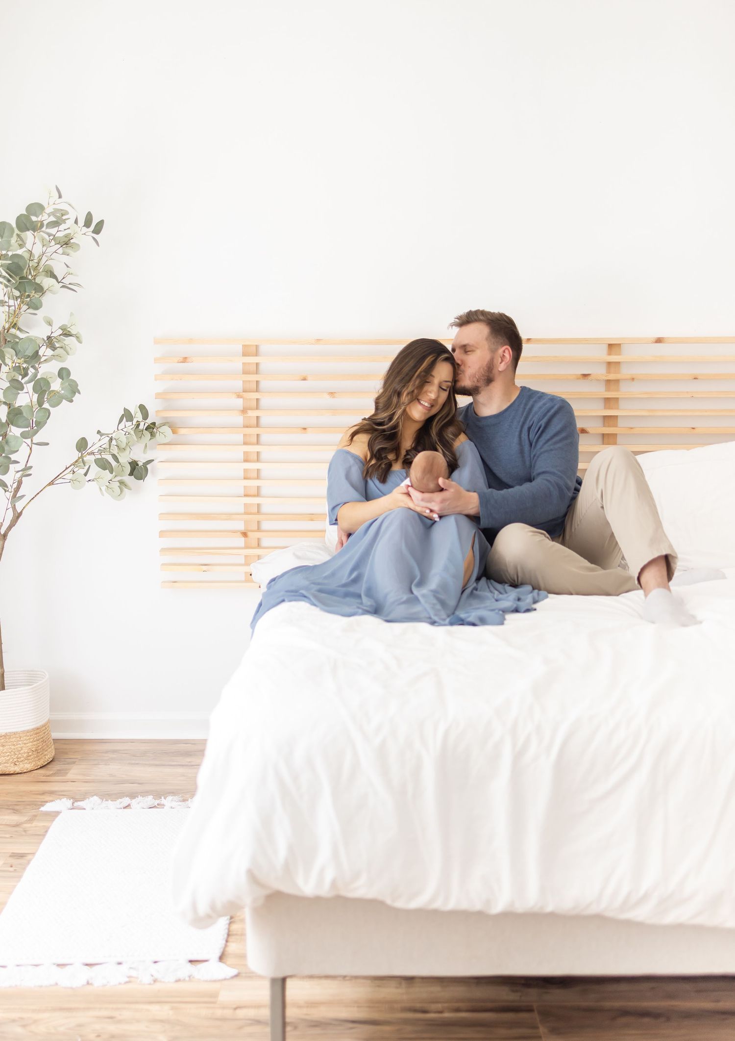 Portrait of new parents sitting on a white bed holding their newborn by Columbus, GA newborn photographer.