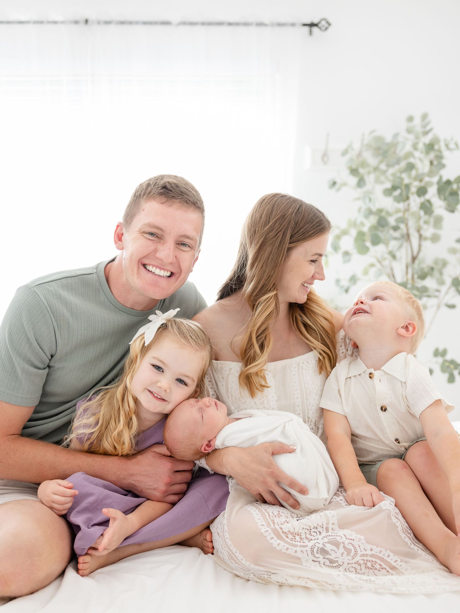 Happy family of five posing for a newborn photo session with two toddlers and a baby in a bright white studio.