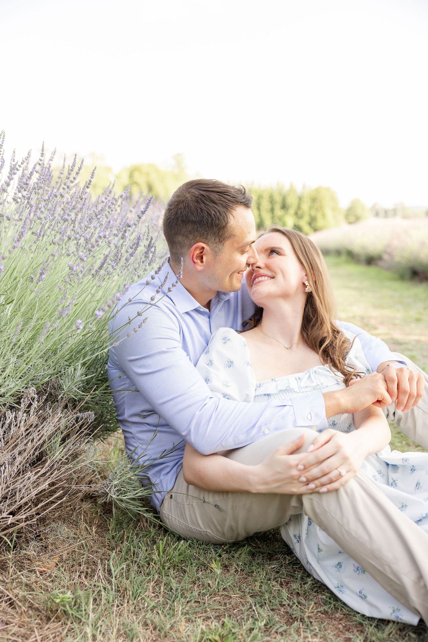 A romantic couple sits together in a lavender field on a beautiful evening celebrating their engagement with their Columbus, GA photographer