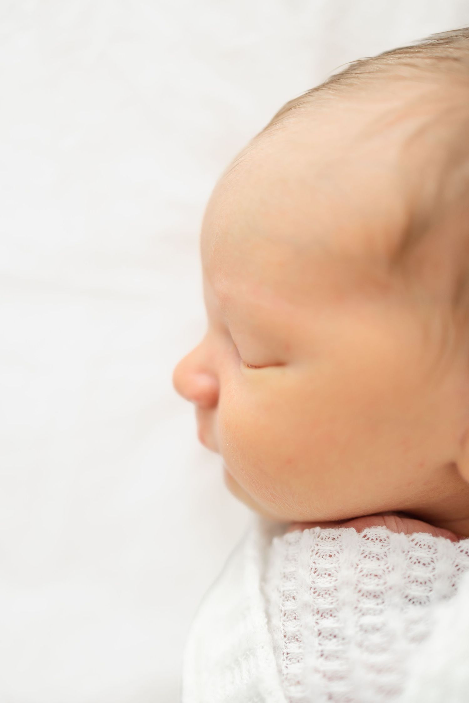 A sleeping newborn baby swaddled in white at his newborn photography session in Columbus, GA.