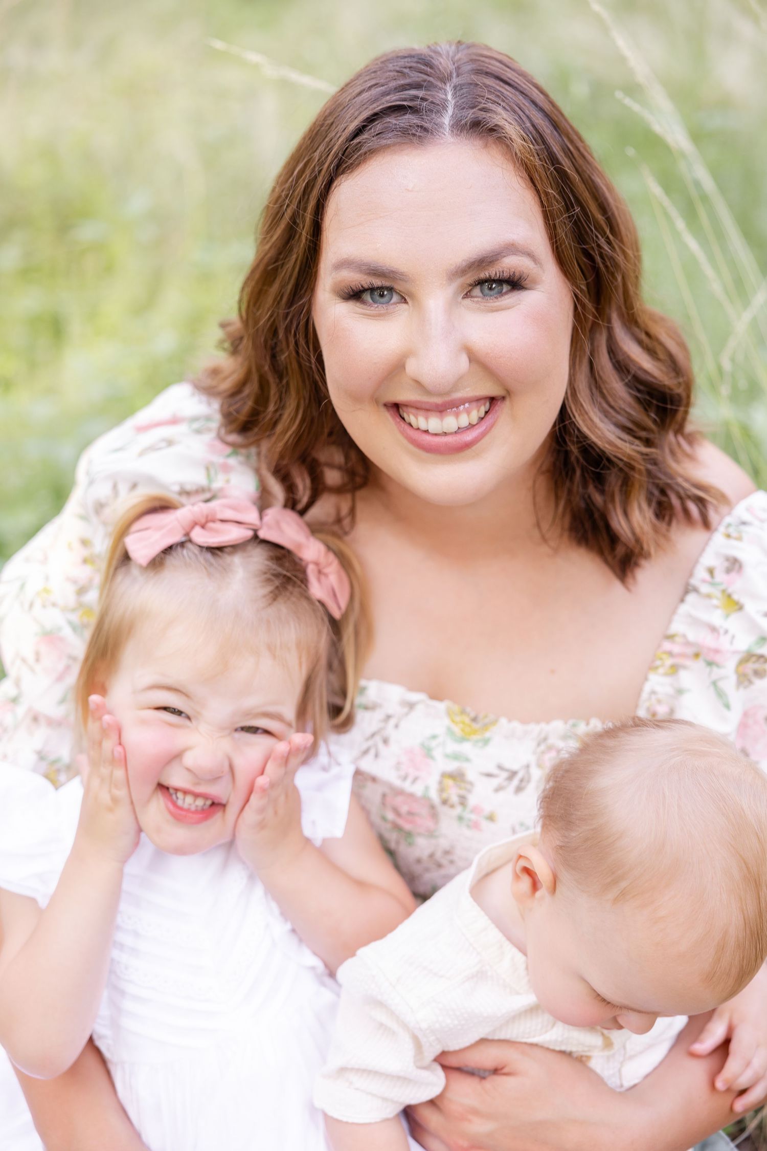 A mother and her children share joyful laughs while posing together in white outfits against a soft light background during family photos.