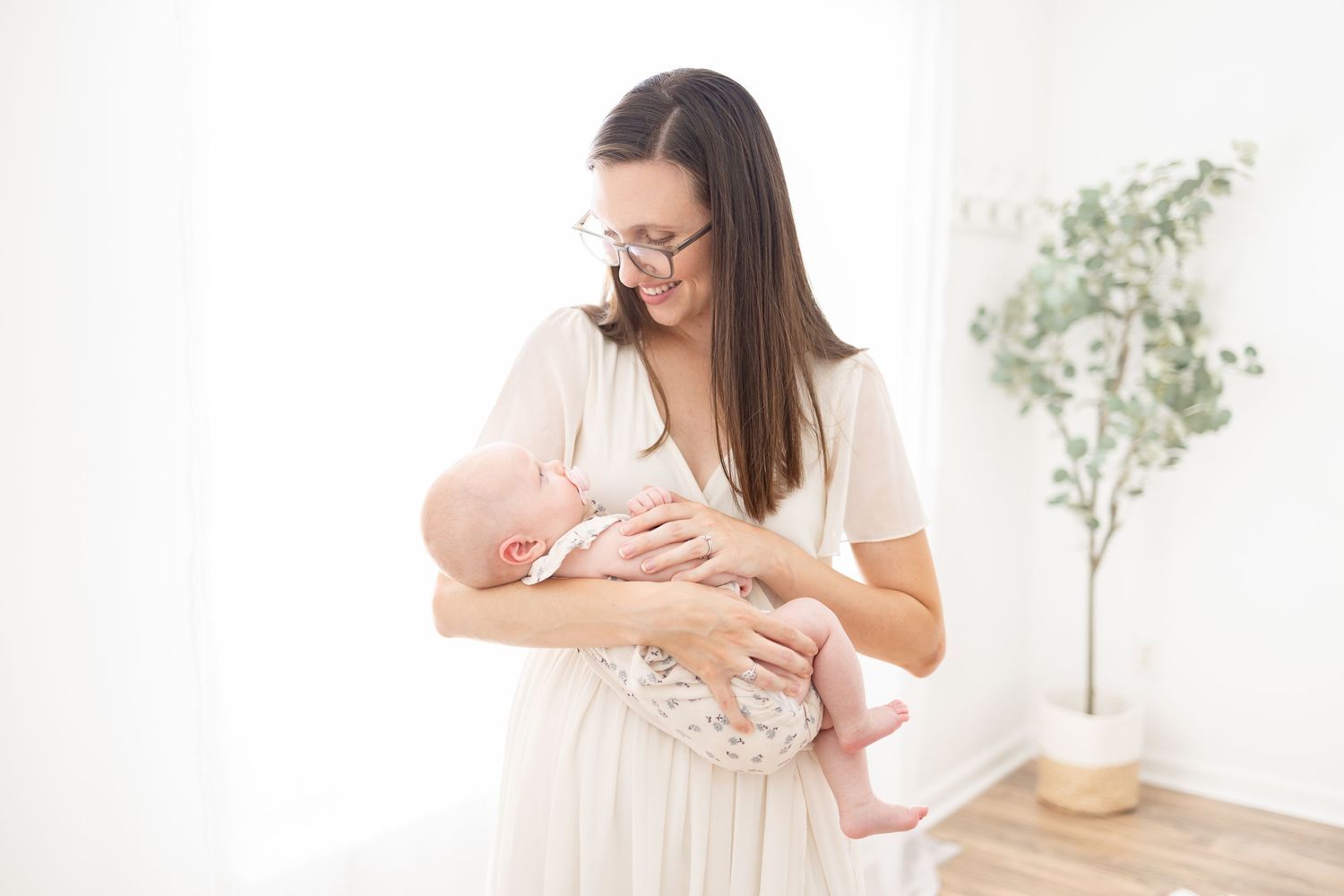 A nurturing parent in a light dress holds and gazes adoringly at a newborn baby in a bright minimalist room.