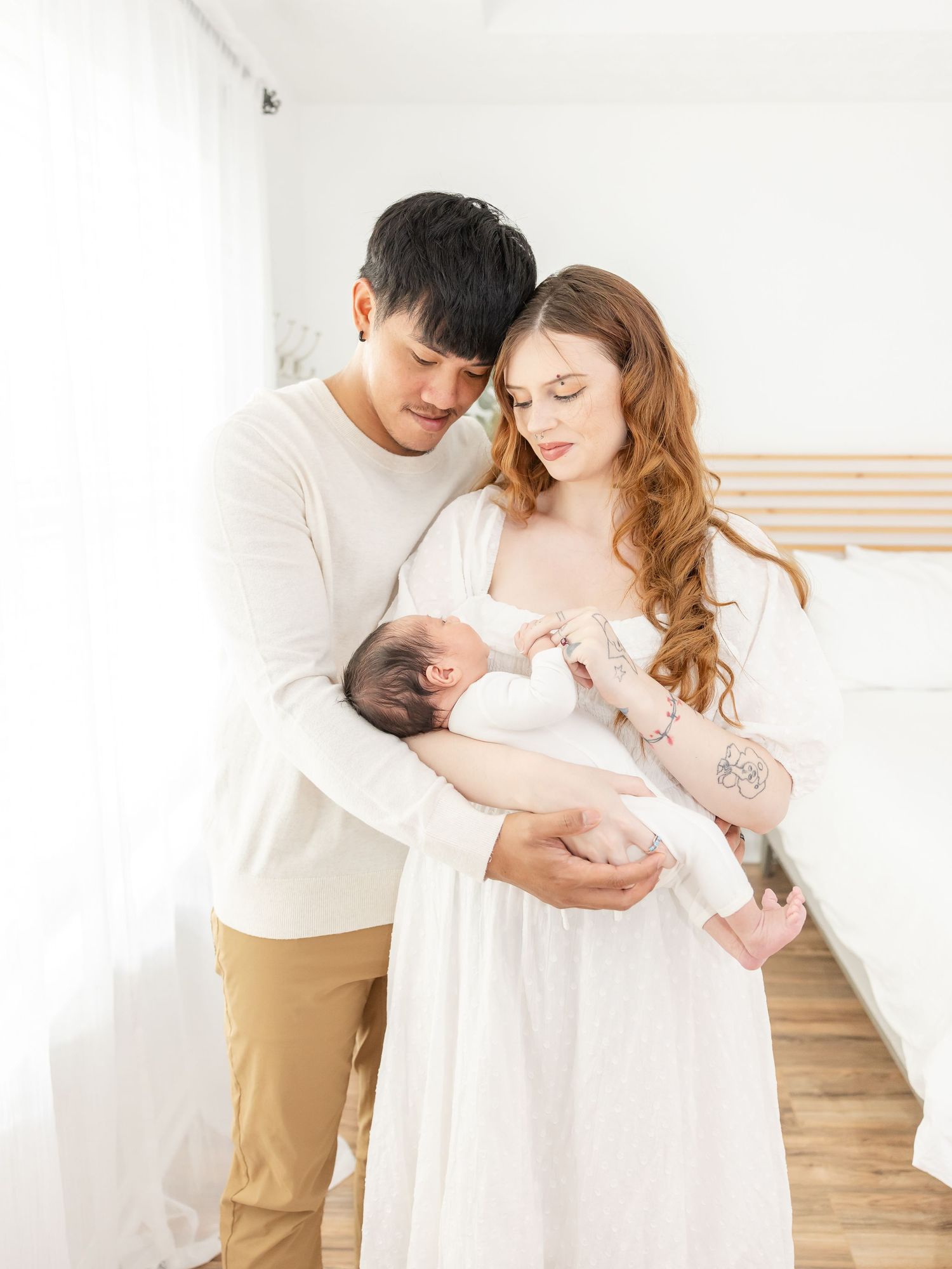 A couple in white clothing shares intimate moments with their newborn at their minimal luxury studio newborn session in Columbus, GA.