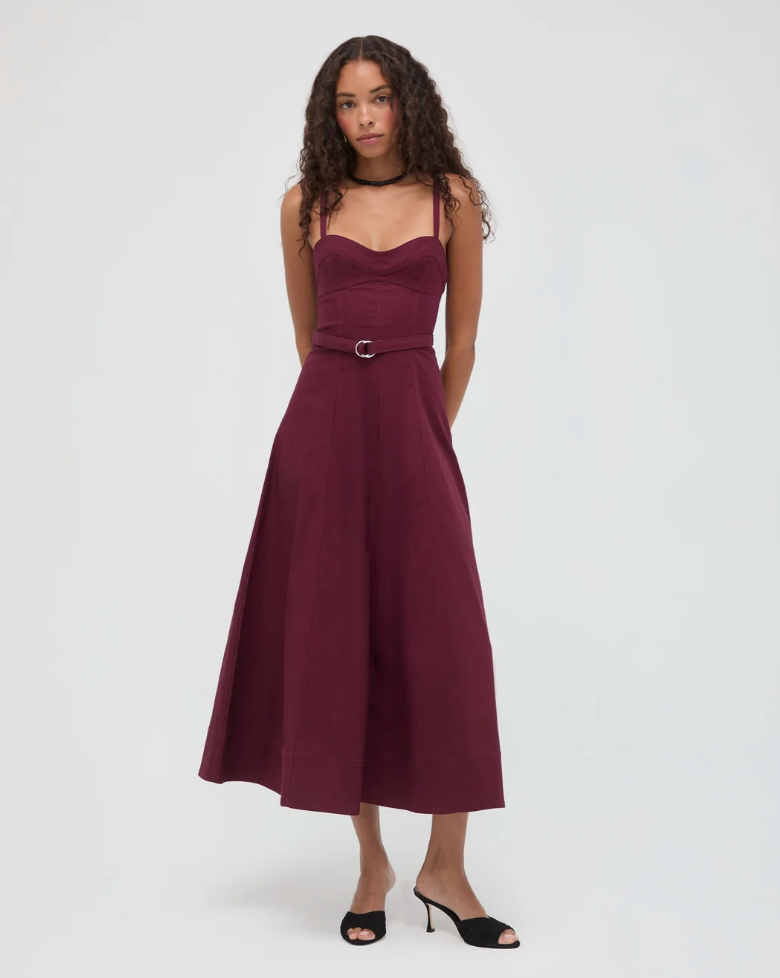 Woman wearing a burgundy sleeveless midi dress with sweetheart neckline, belt detail, and A-line skirt, styled with black heeled mules.