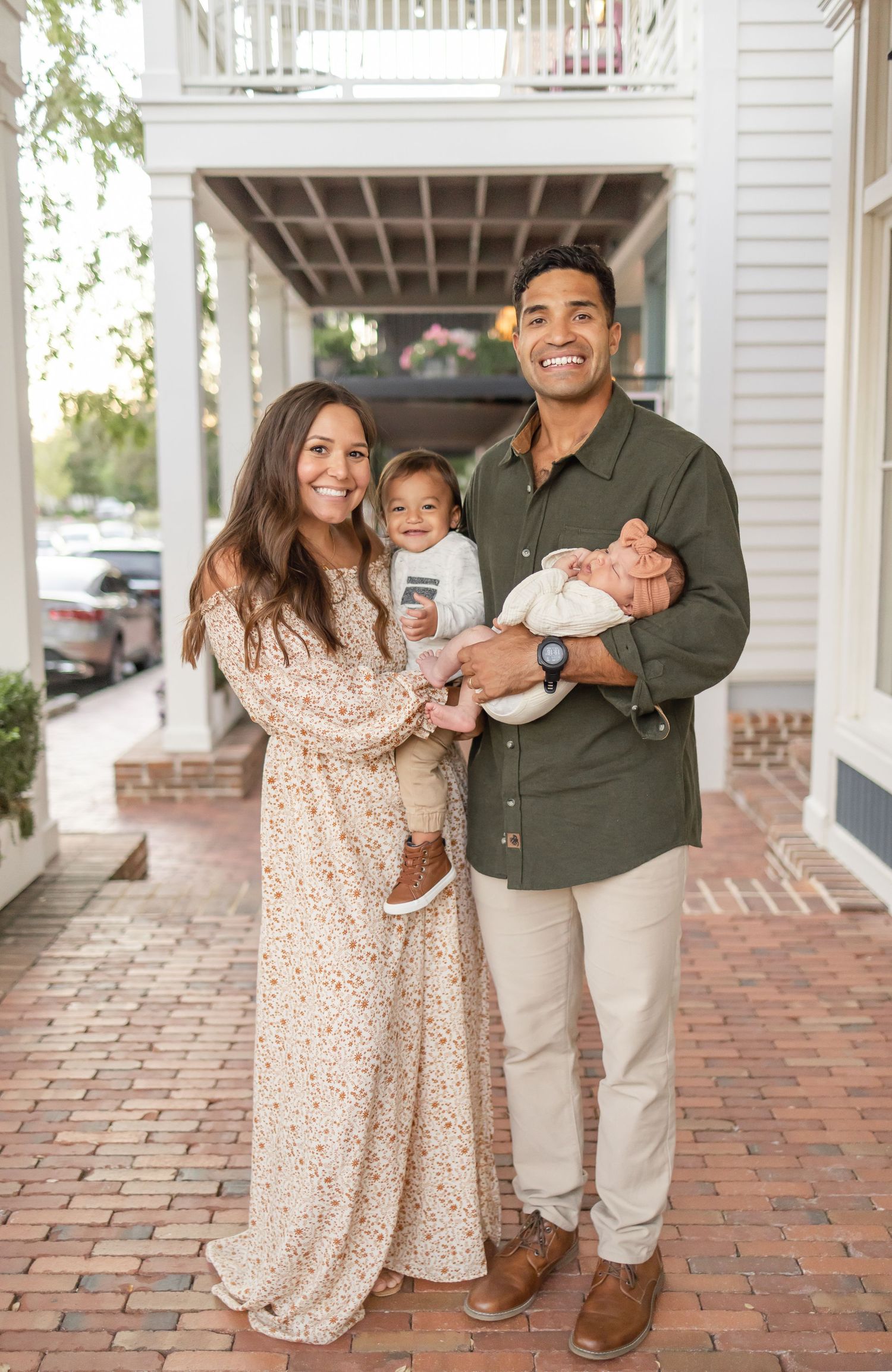 A family stands together on a brick porch sidewalk smiling during their family portrait session by Columbus, GA family photographer.