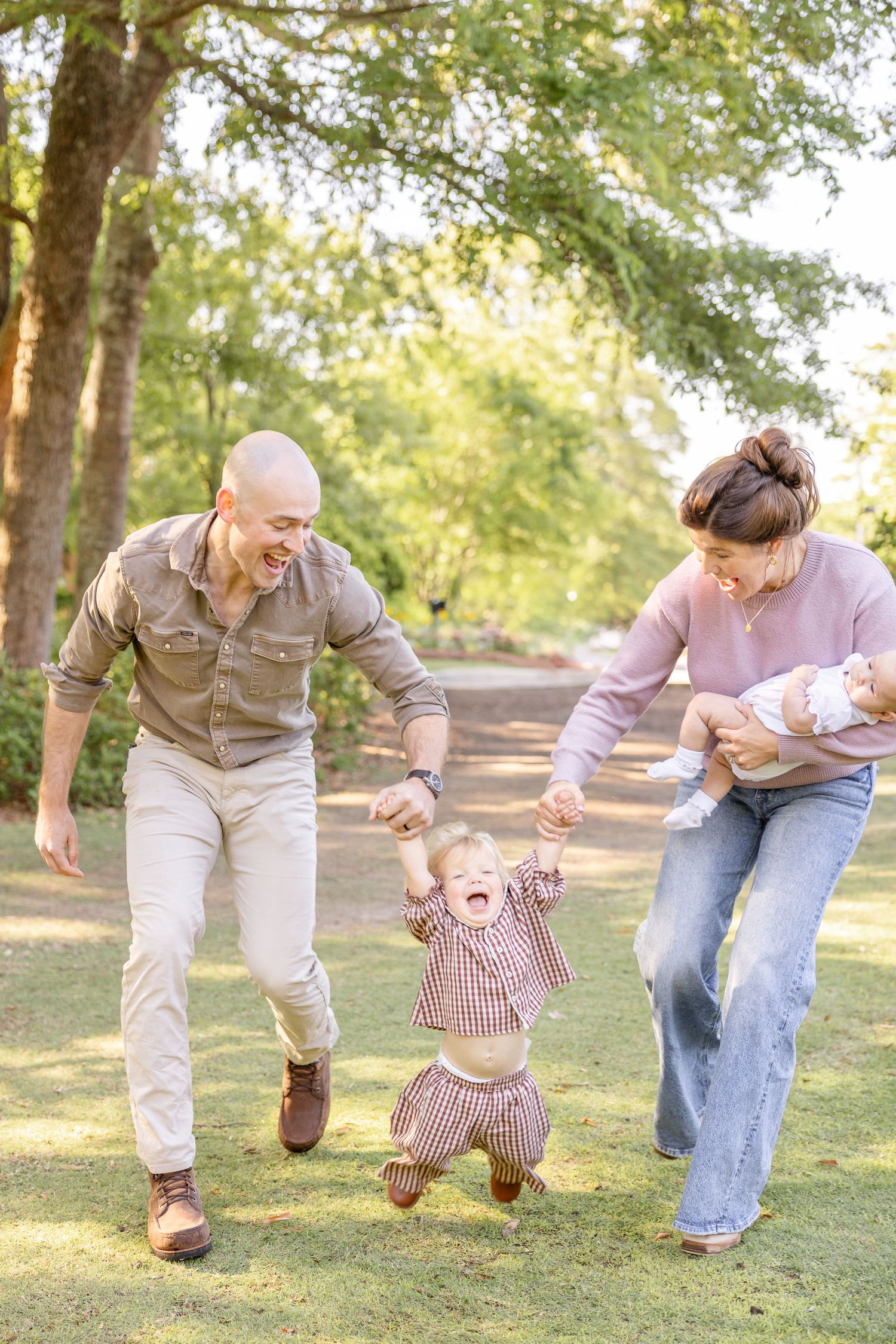 Happy family with toddler and newborn playing outdoors in a lush green park on a sunny day.