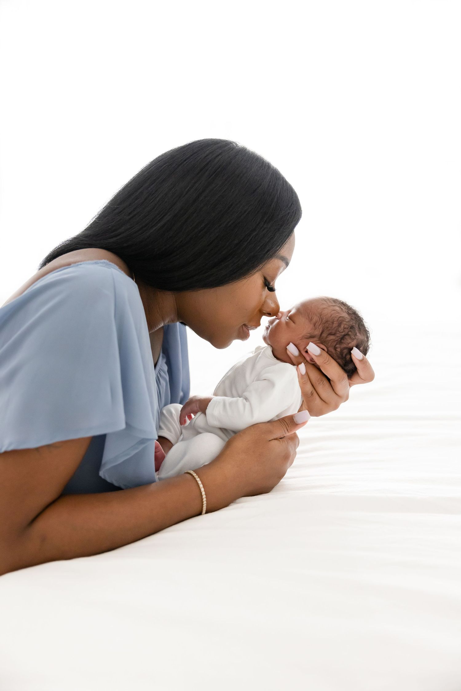 Mother gently touches her baby’s nose with hers against a bright white background at Columbus, GA studio newborn session.