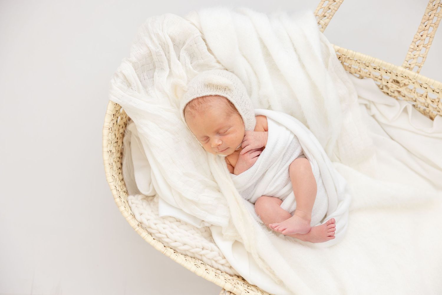 Sleeping newborn baby wrapped in white swaddle blanket lying in vintage wicker bassinet by Columbus, GA newborn photographer.