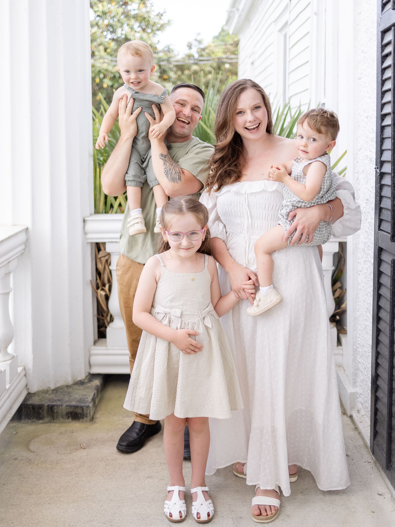 Happy family of five posing on a white porch, parents holding toddlers while young girl stands in the middle by Columbus, GA photographer.