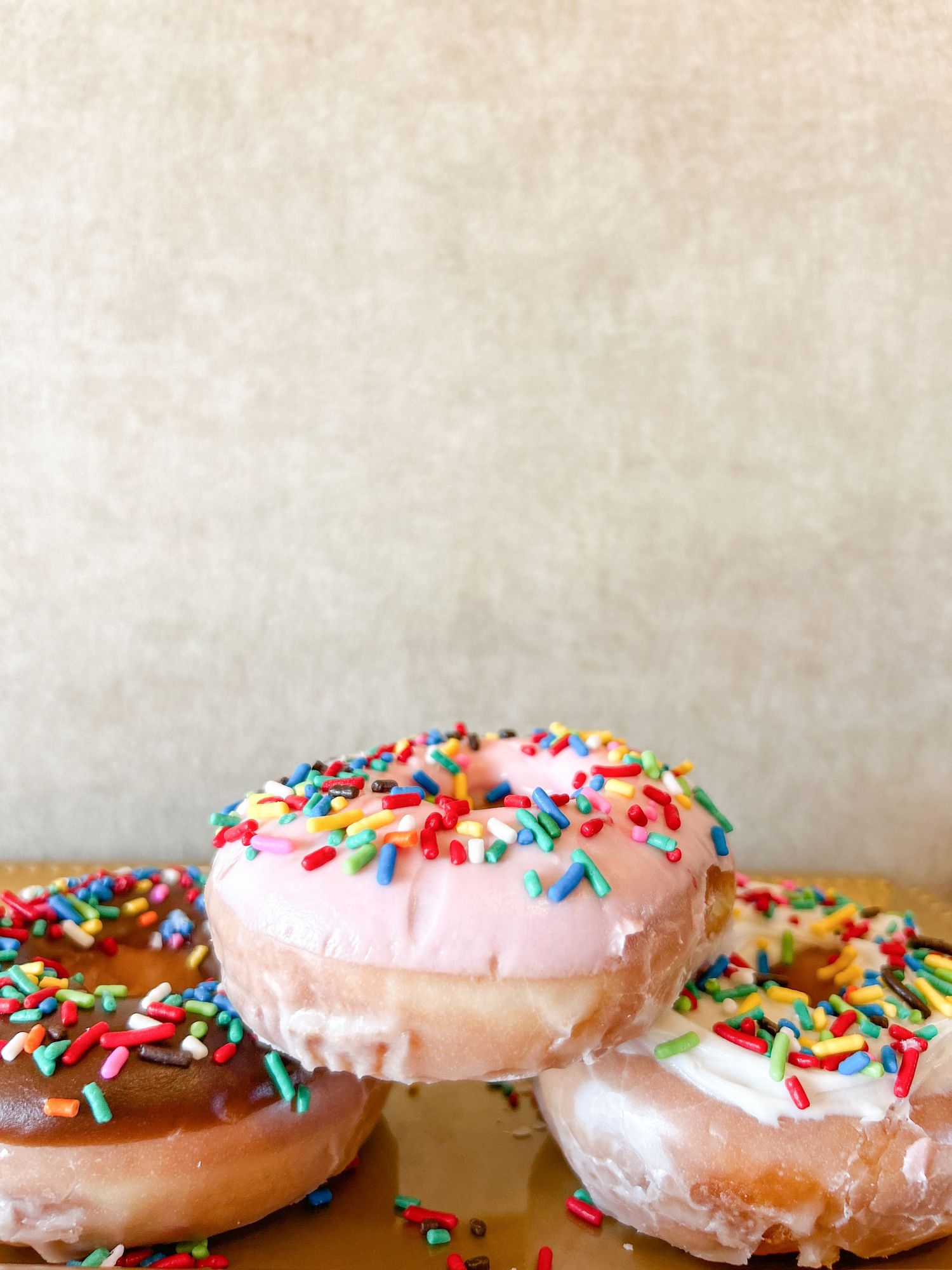 Pink frosted donuts with colorful rainbow sprinkles arranged in a row on a wooden surface. Golden Donuts Columbus, GA