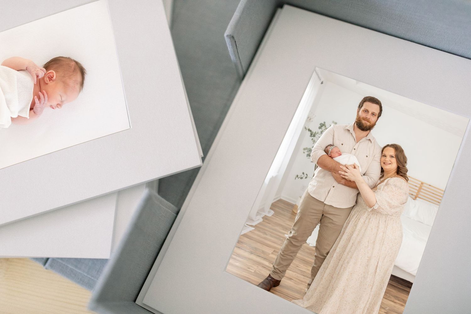 Photos arranged on a white surface show a newborn baby photo and a family portrait in soft neutral tones.