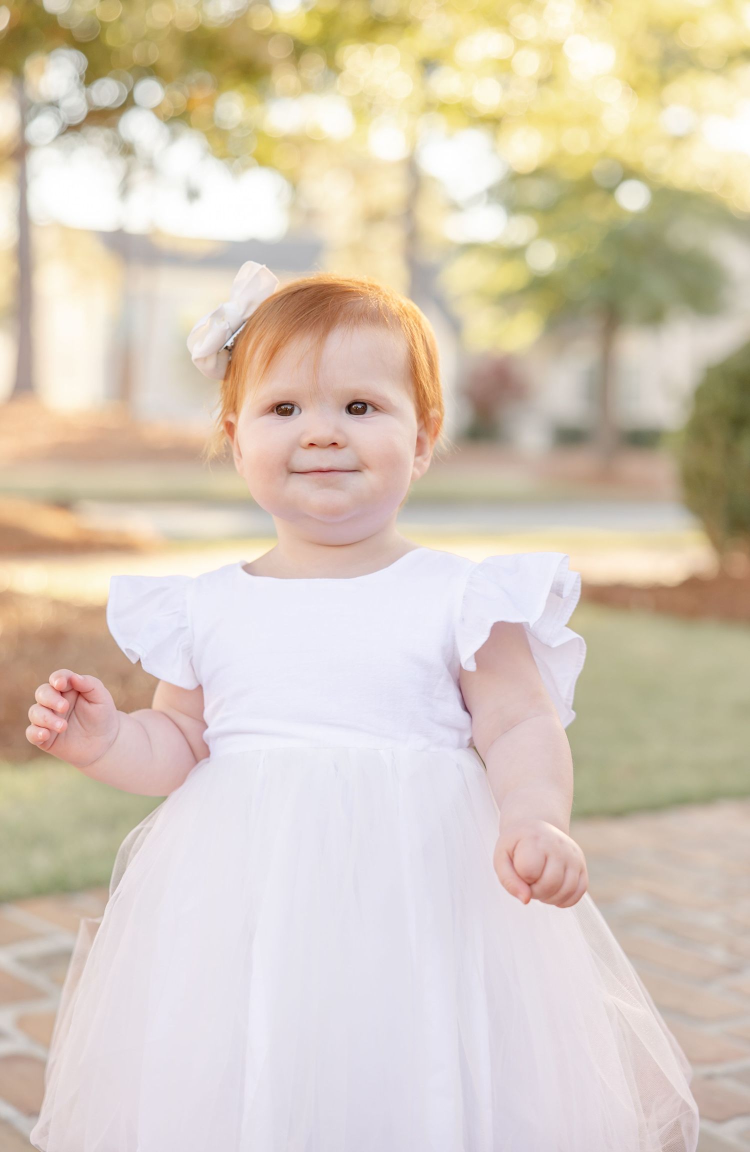 A little girl in a white dress with flutter sleeves twirls and plays outdoors during golden hour at her family photo session in Columbus, GA