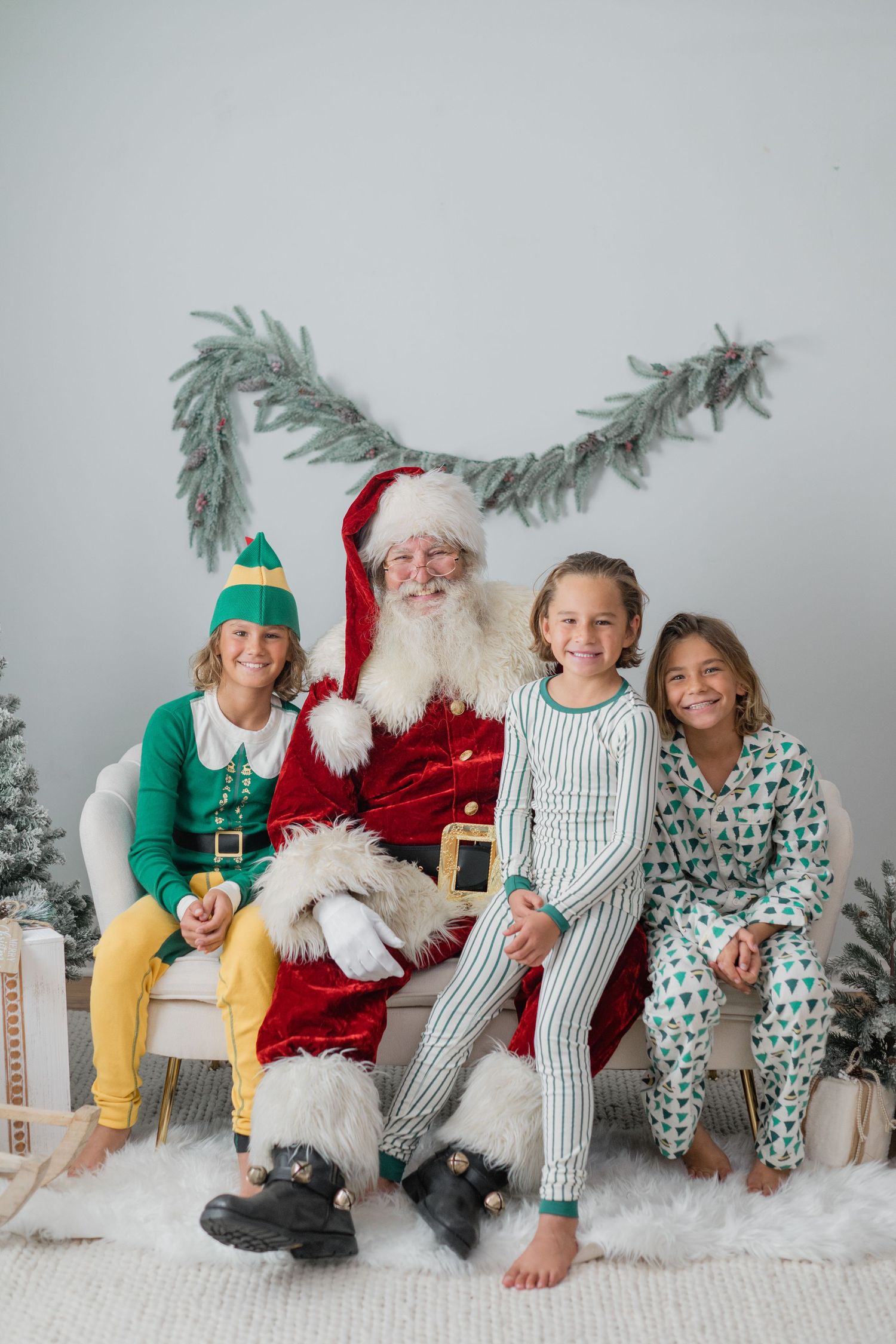 Three children in Christmas pajamas pose with Santa Claus on a couch surrounded by festive holiday decorations.