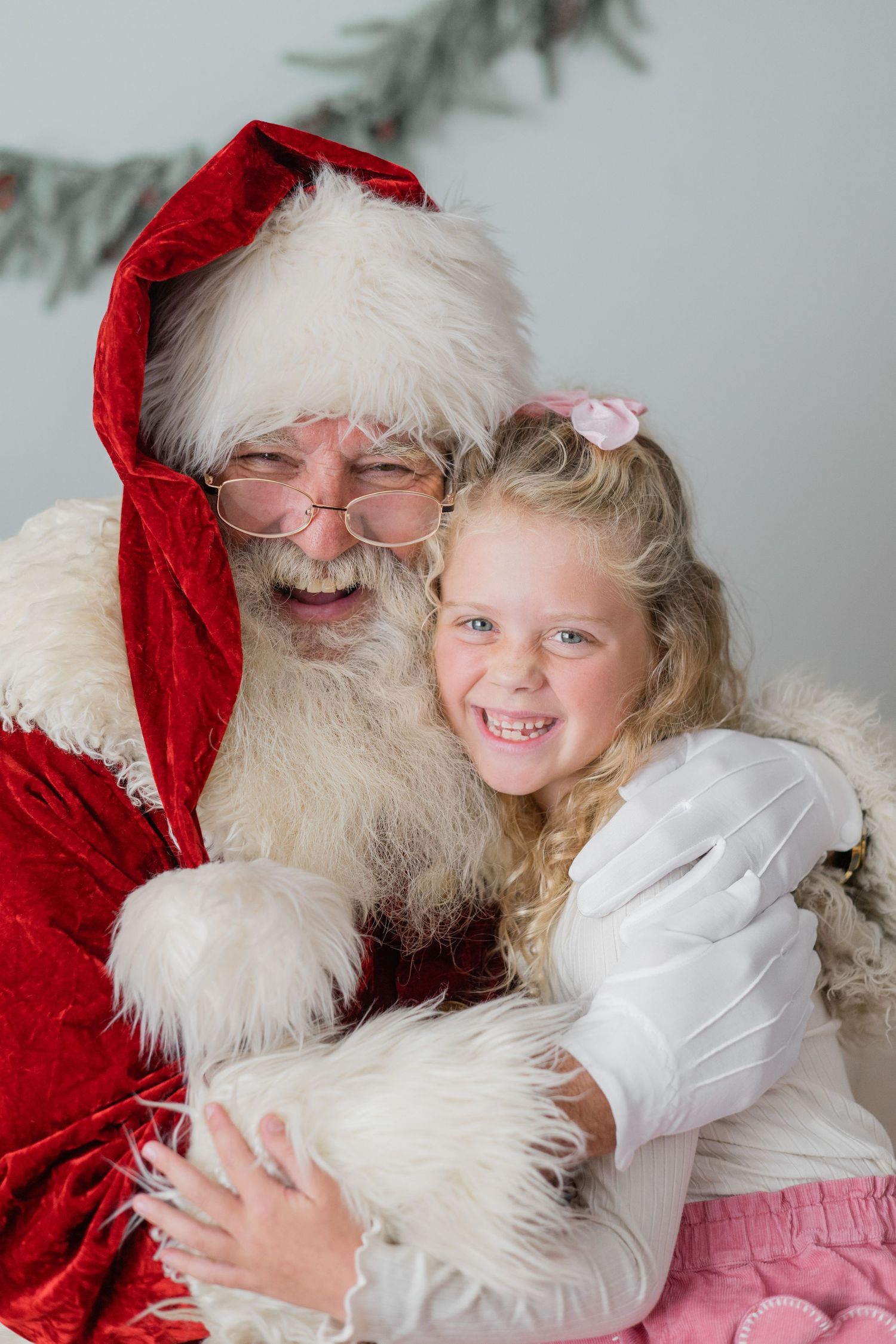 A joyful young girl hugs Santa Claus, both smiling warmly during a festive Christmas portrait session.