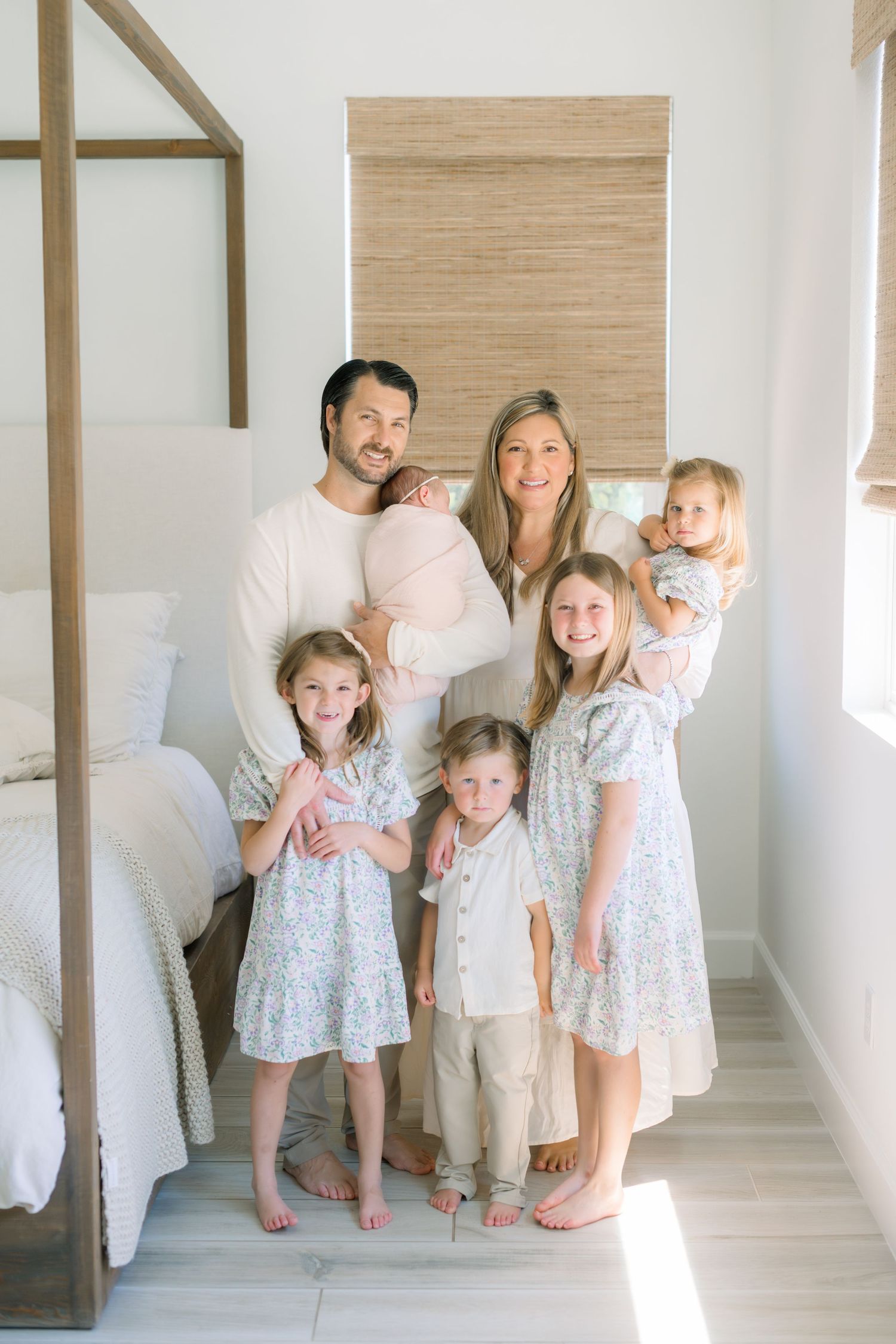 A family of seven poses indoors, parents holding two children, with four kids standing, dressed in neutral tones.