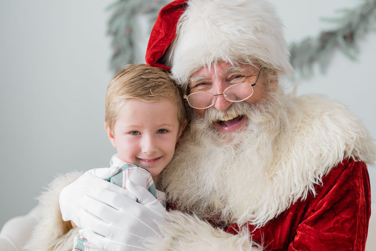 A young boy smiling with Santa Claus in a warm holiday portrait, both sharing a joyful hug.