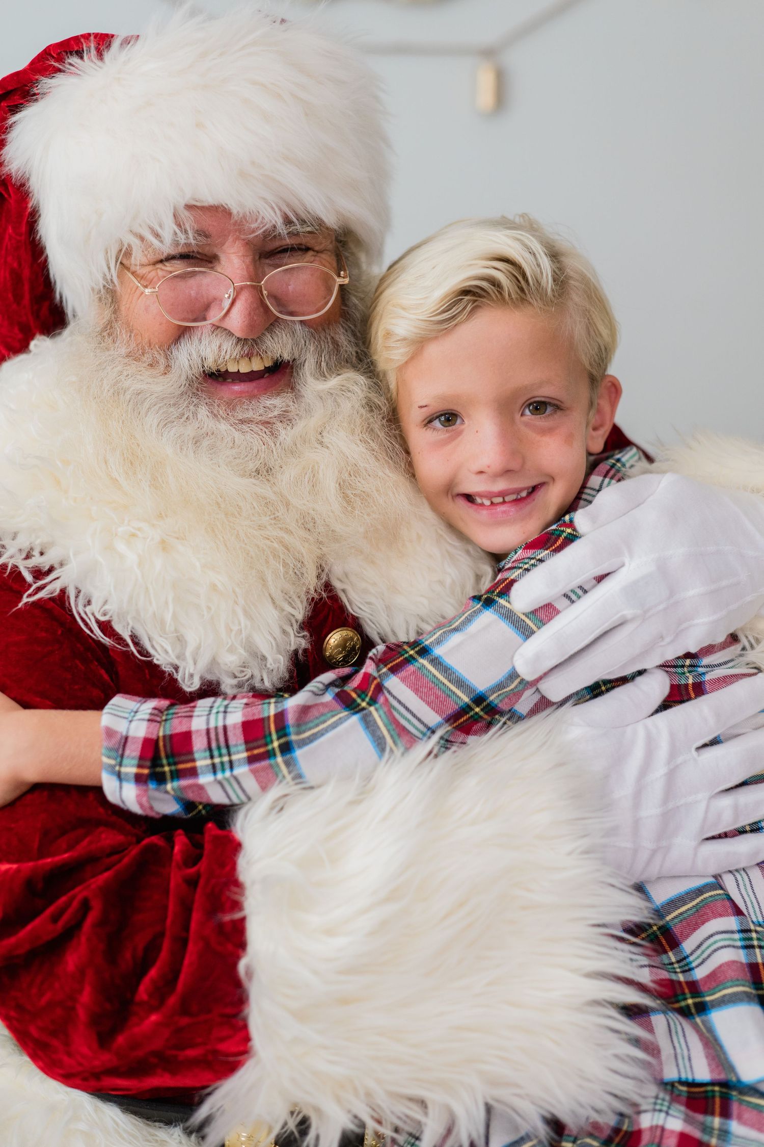 Smiling boy in plaid pajamas hugging Santa Claus during a festive Christmas portrait session.