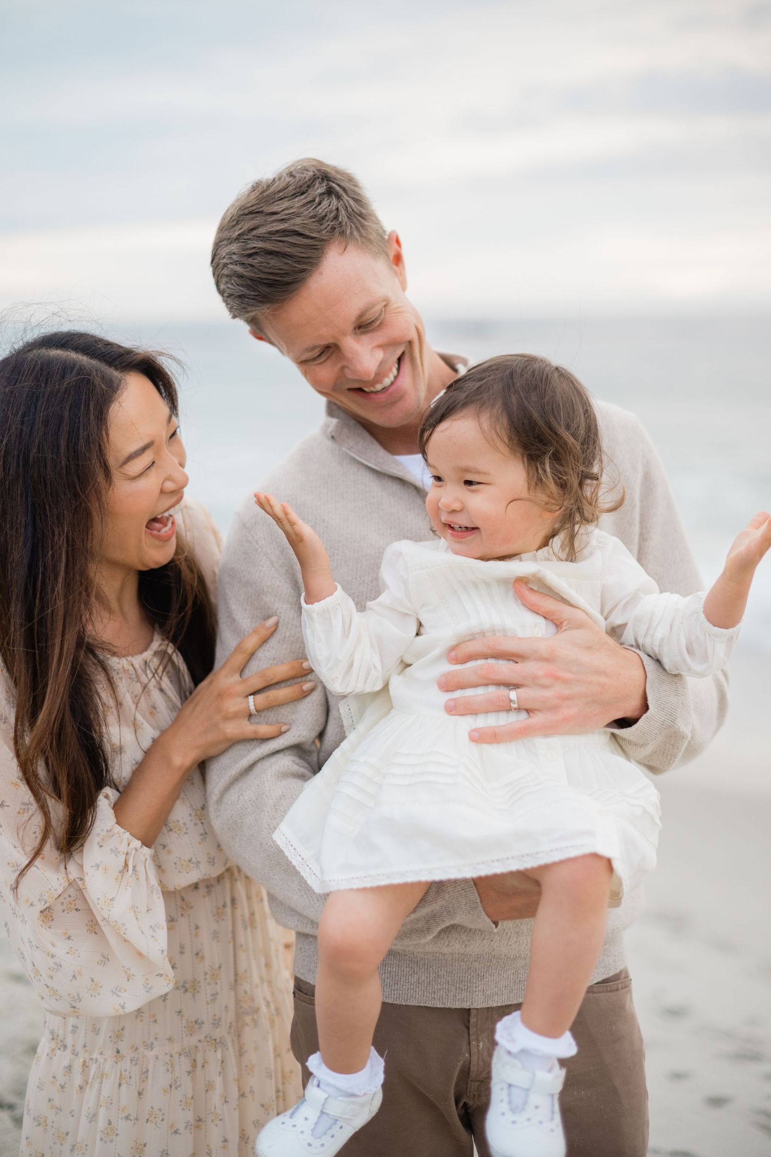 Happy interracial family with smiling parents holding their joyful baby girl on a beach.