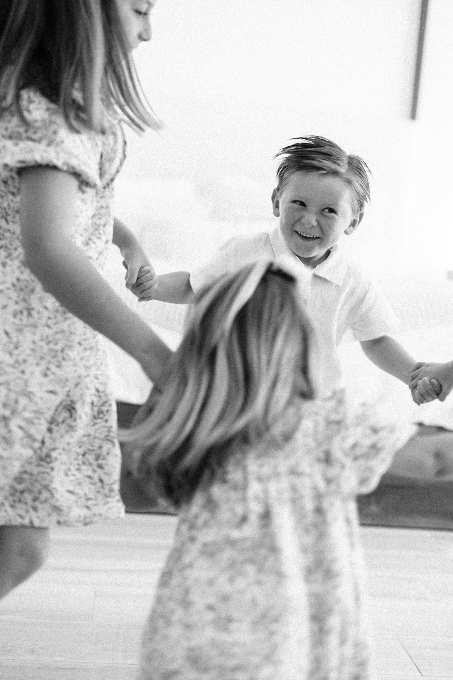 Black and white photo of three children holding hands and spinning in a circle, laughing joyfully indoors.