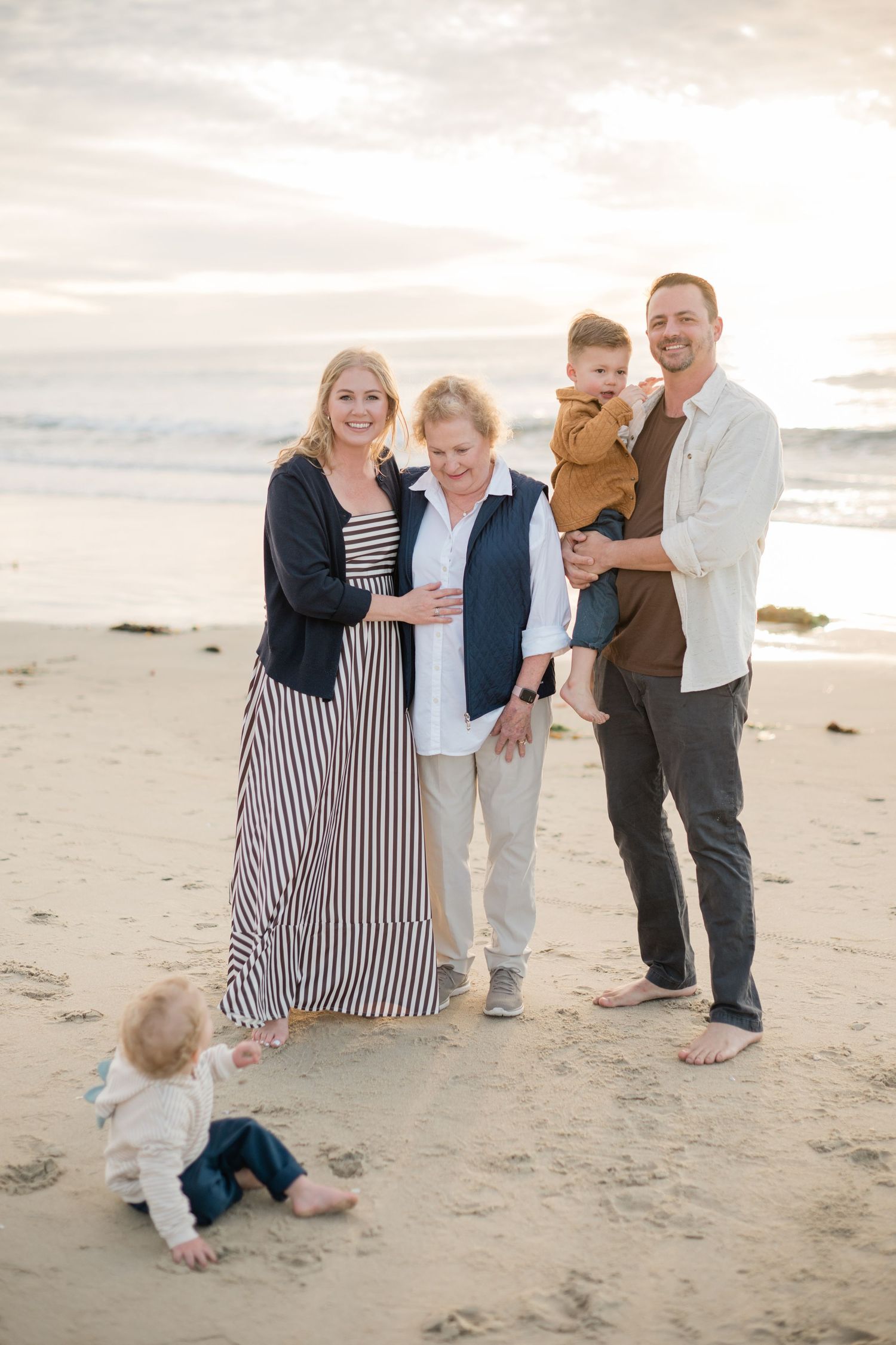 Family of five posing on a sandy beach at sunset, with two young children and three smiling adults.