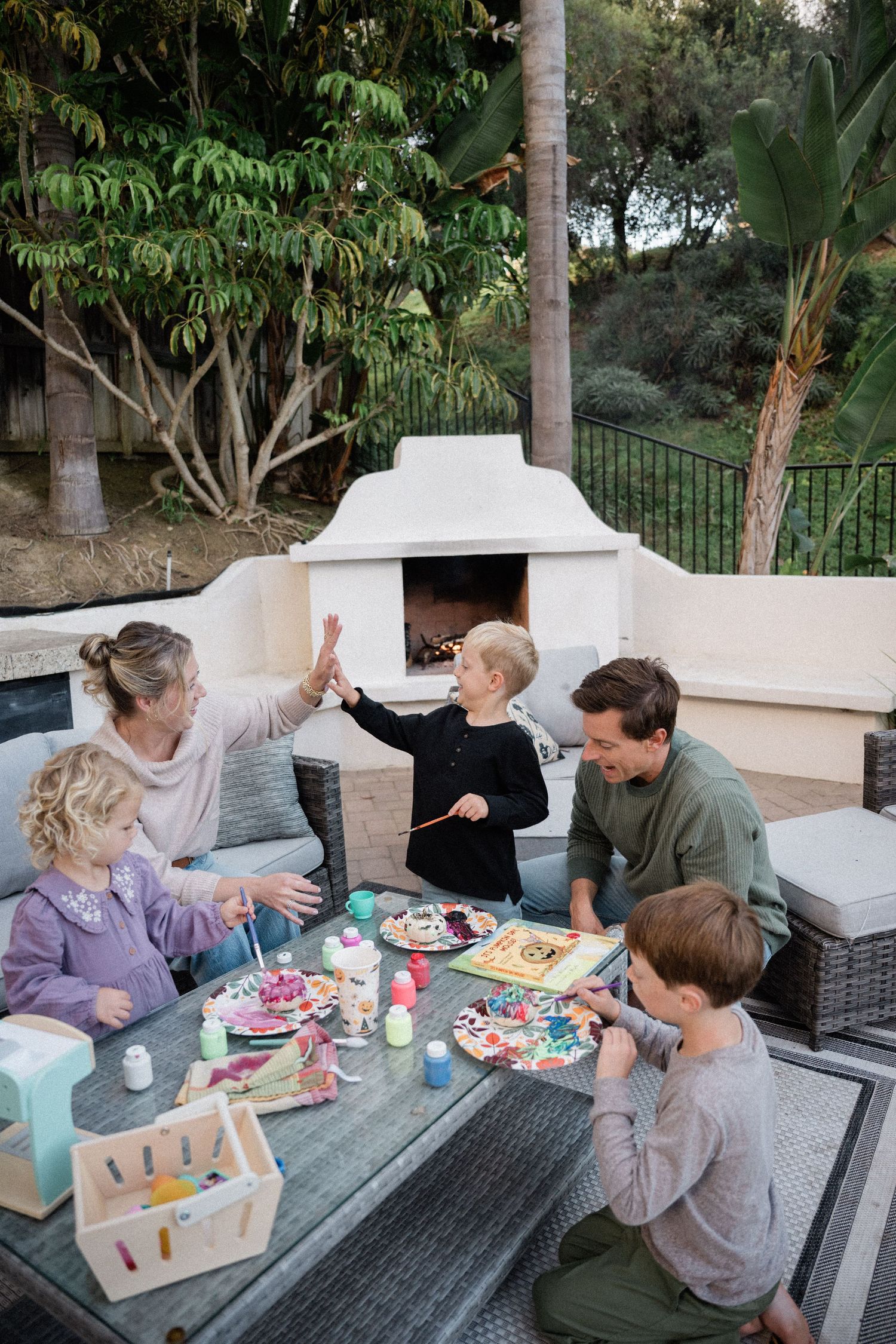 Family of five doing arts and crafts together at outdoor patio table near fireplace.