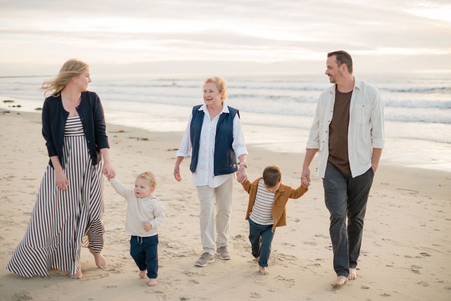 Family of five walking on a sandy beach at sunset, holding hands and smiling together.