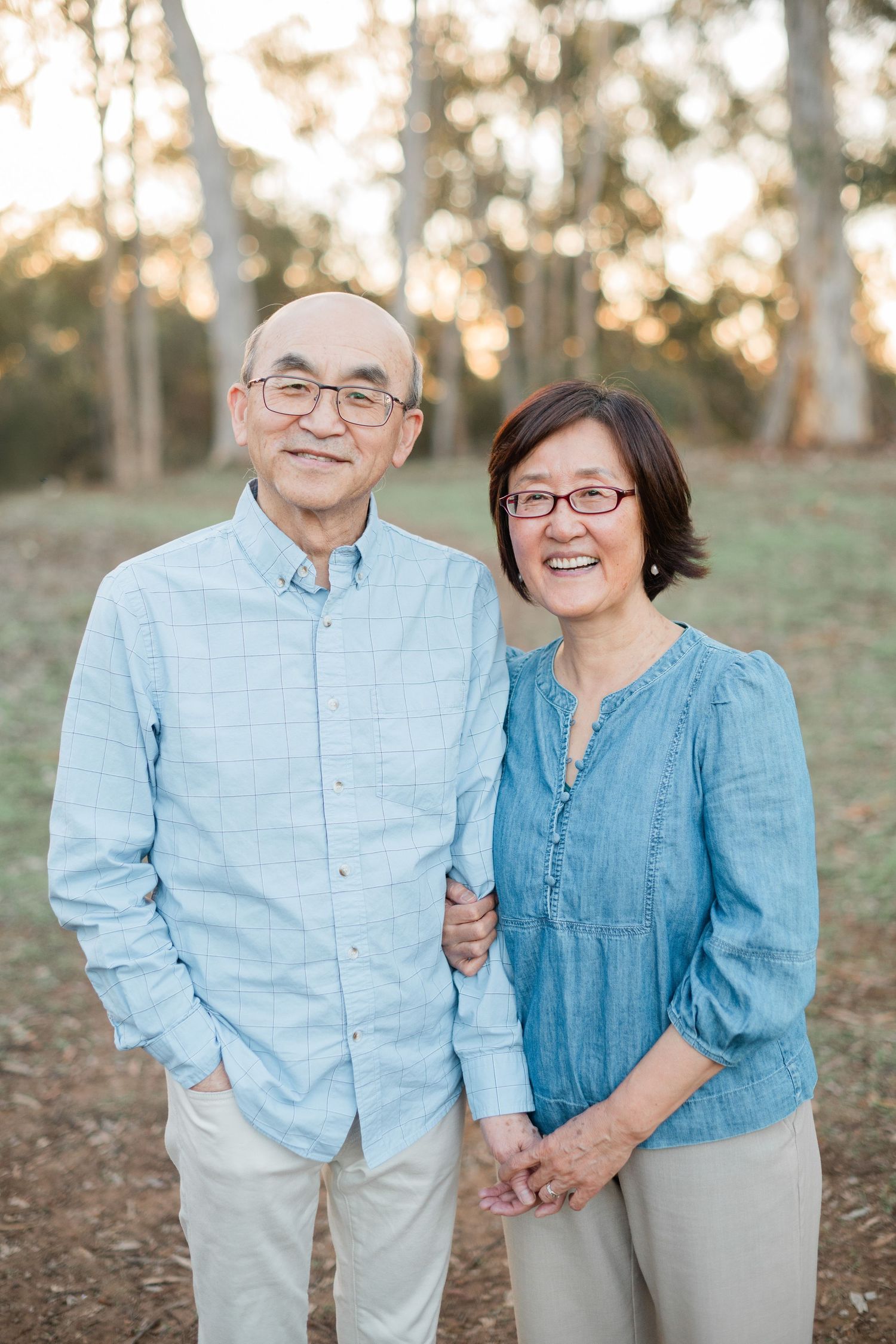Happy Asian senior couple smiling together outdoors among trees in a warm family portrait.