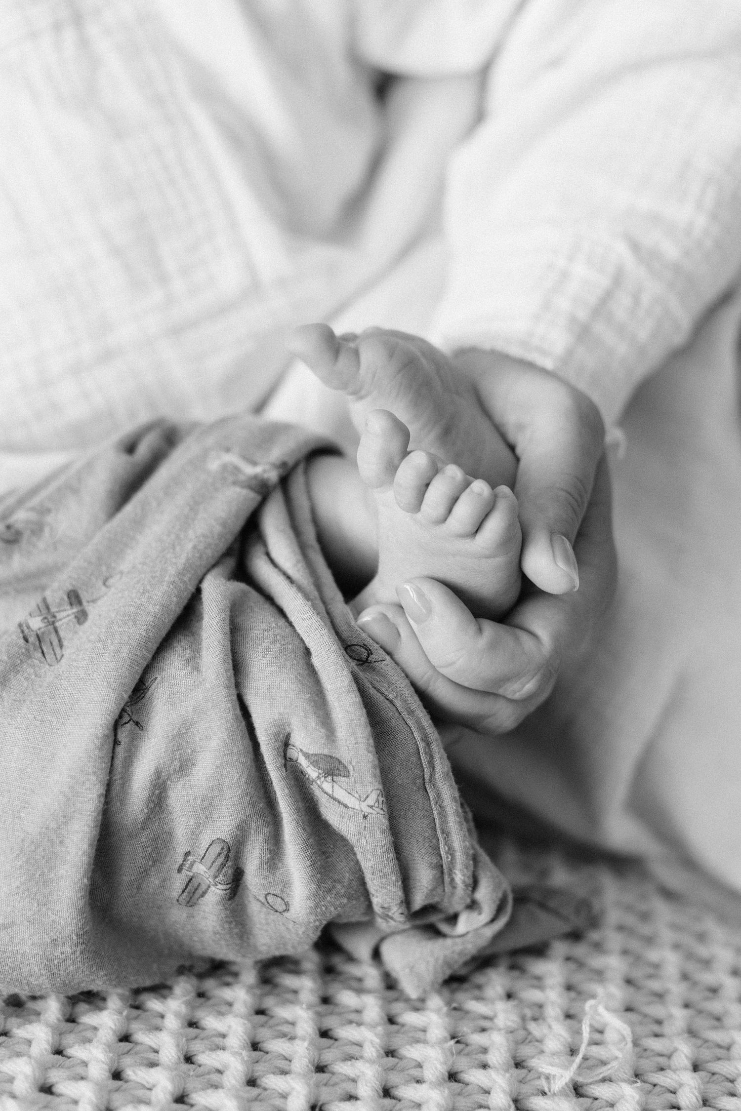Black and white macro photo of a newborn baby's tiny feet resting on a soft patterned blanket.