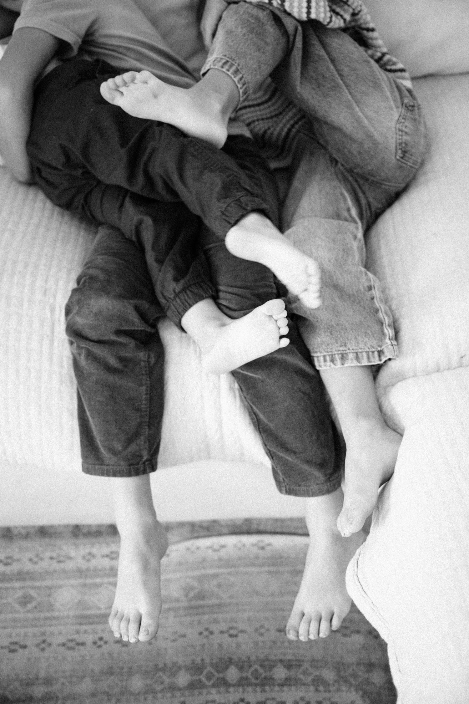 Black and white photo of children and adult sitting barefoot on a couch together.
