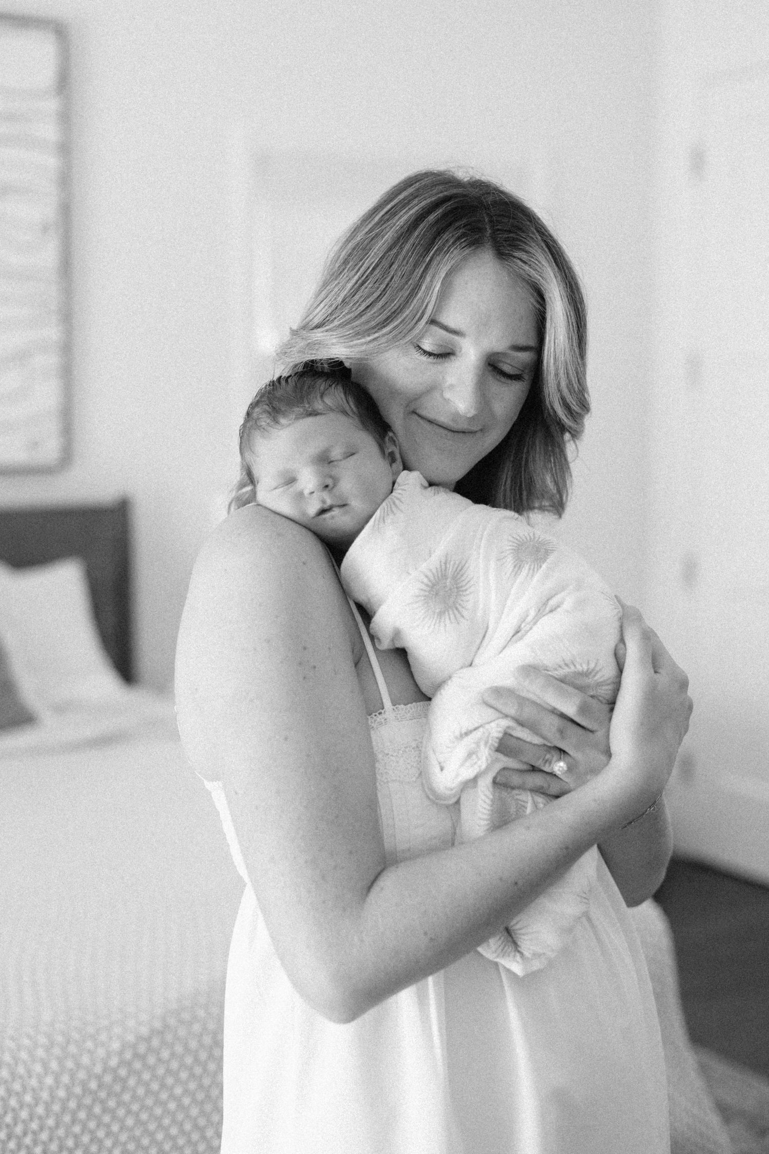 Black and white photo of mother tenderly holding sleeping swaddled newborn baby.