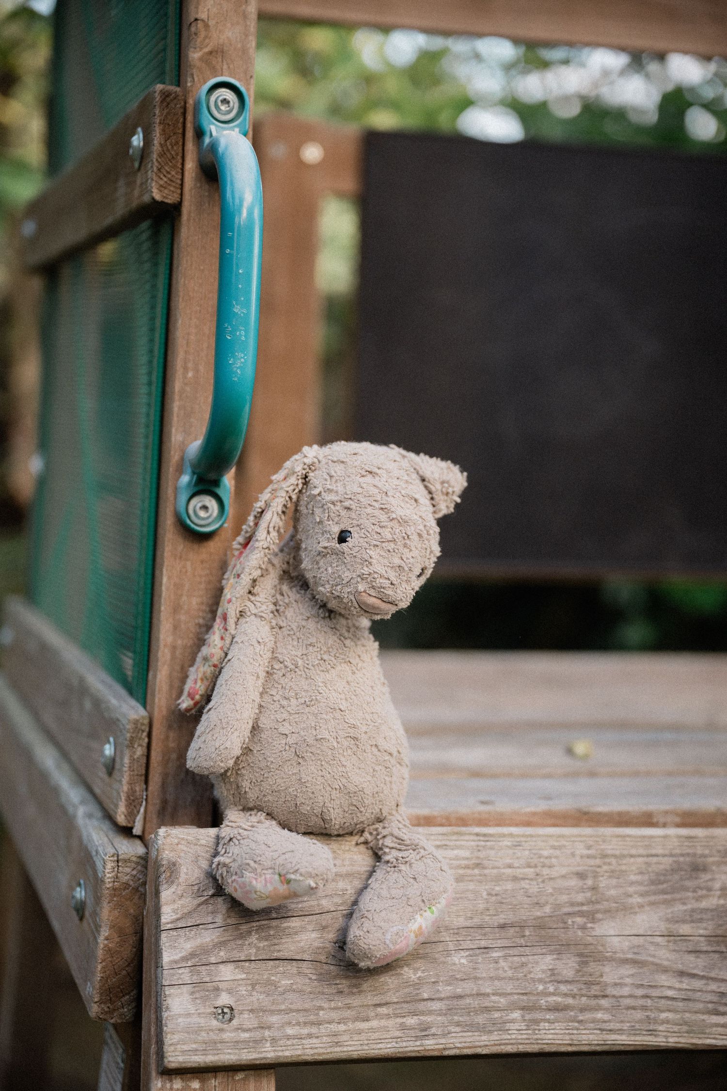 A worn stuffed bunny rabbit toy sitting alone on a wooden playground structure ledge.