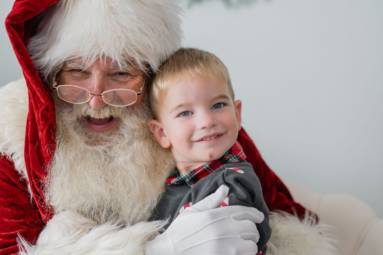 A young smiling boy sits on Santa Claus's lap, both happy during a festive Christmas photo session.