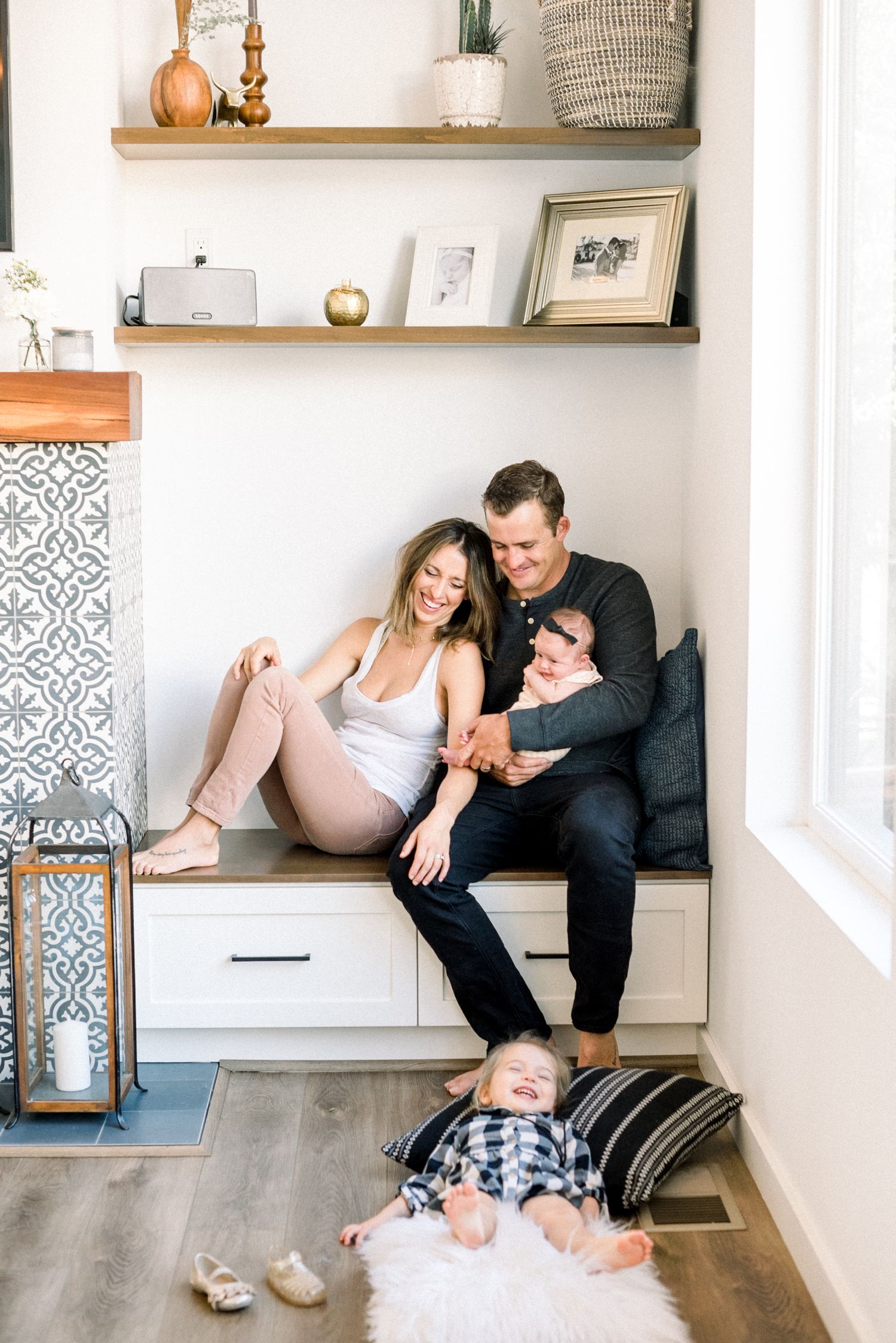 Happy family with a newborn and laughing toddler relaxing on a built-in bench beside a decorative fireplace.