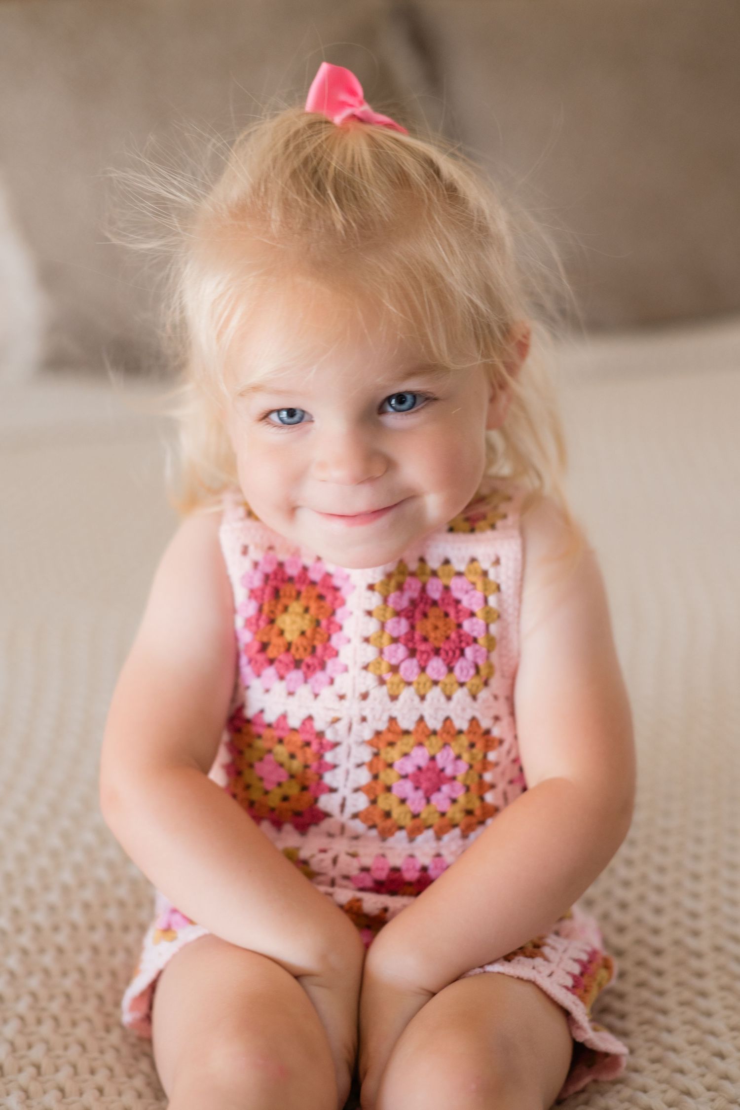 Adorable blonde toddler girl smiling in pink crochet granny square dress.
