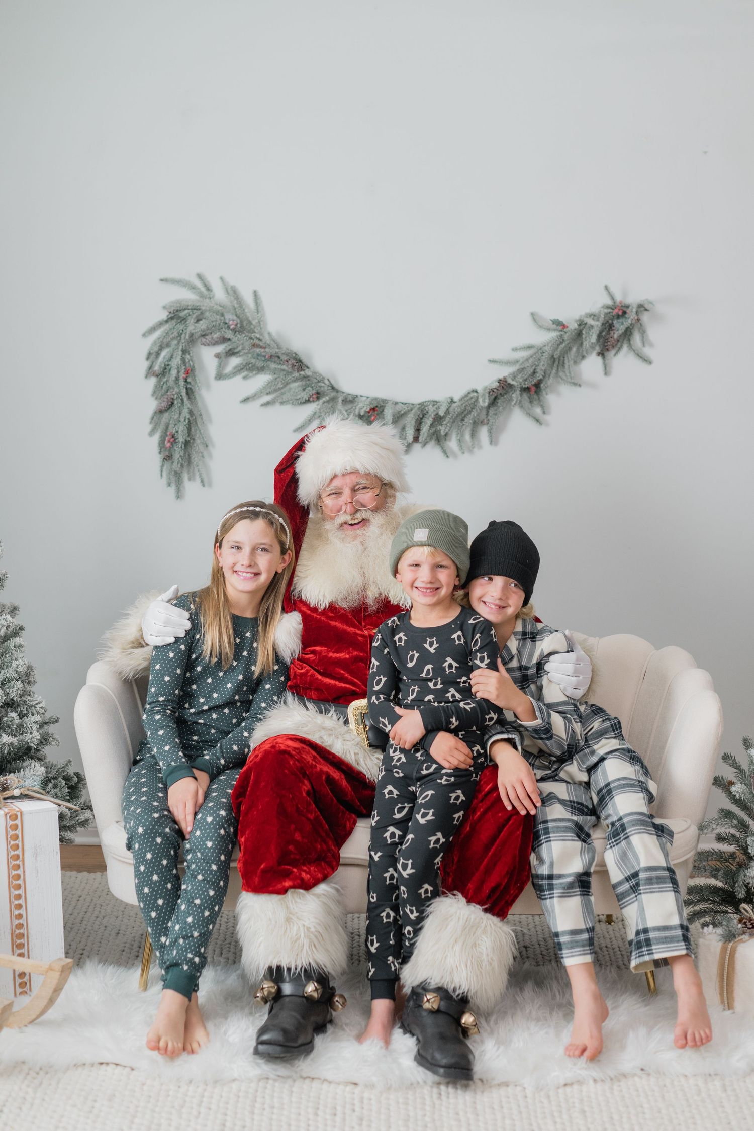 Three children in pajamas posing with Santa Claus on a cozy chair in a Christmas setting.