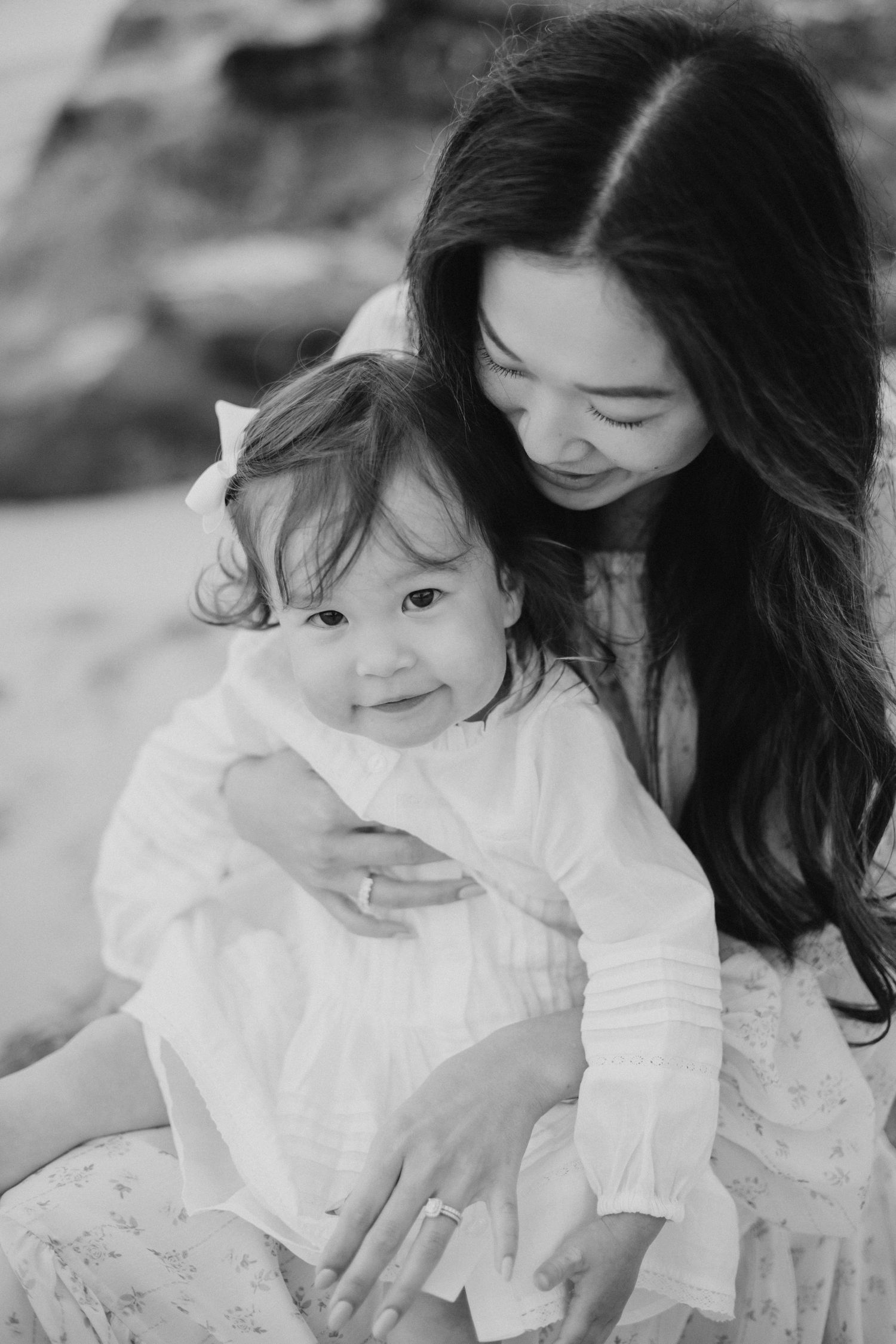 Black and white photo of a mother tenderly holding her smiling toddler daughter on a beach.