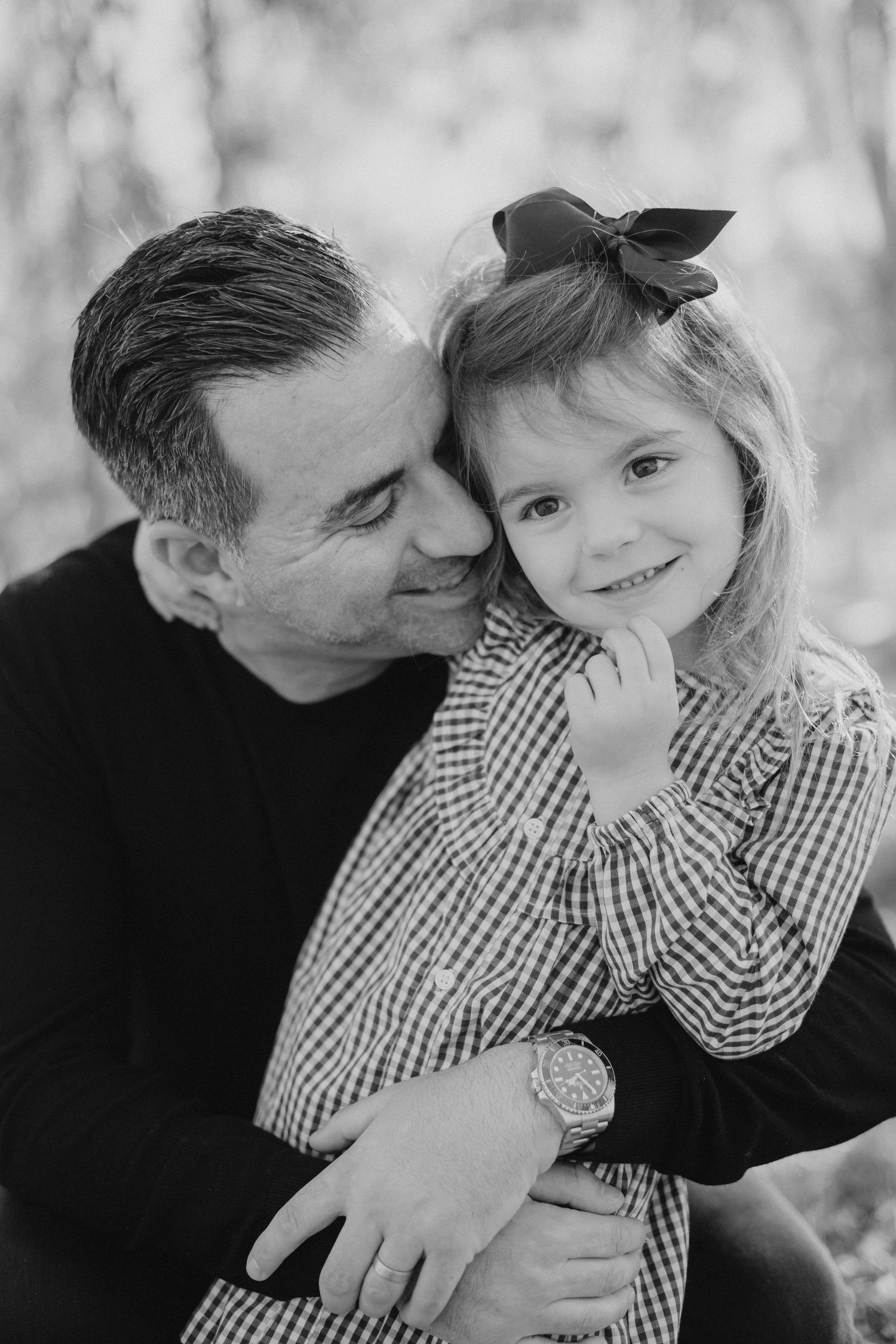 A black and white portrait of a father tenderly embracing his smiling young daughter outdoors.
