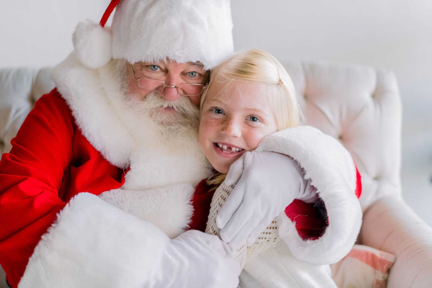 A cheerful young girl smiles with Santa Claus in a warm holiday portrait, wearing festive white attire.