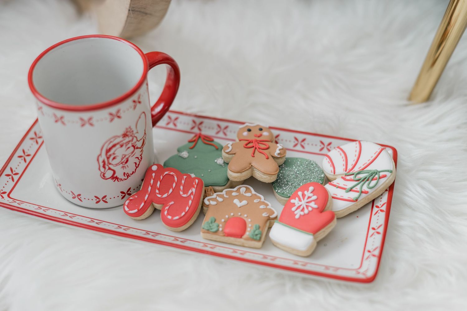 Festive Christmas sugar cookies on a holiday tray with a red and white mug on a white fur surface.