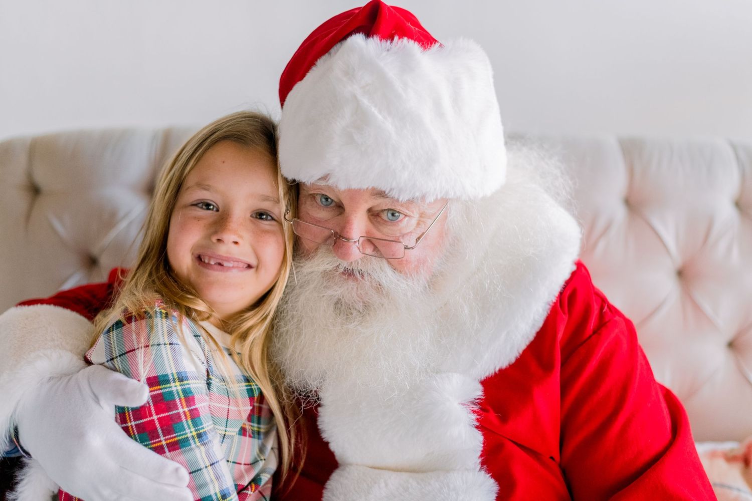 A young girl smiles while posing with Santa Claus in a cozy holiday setting.