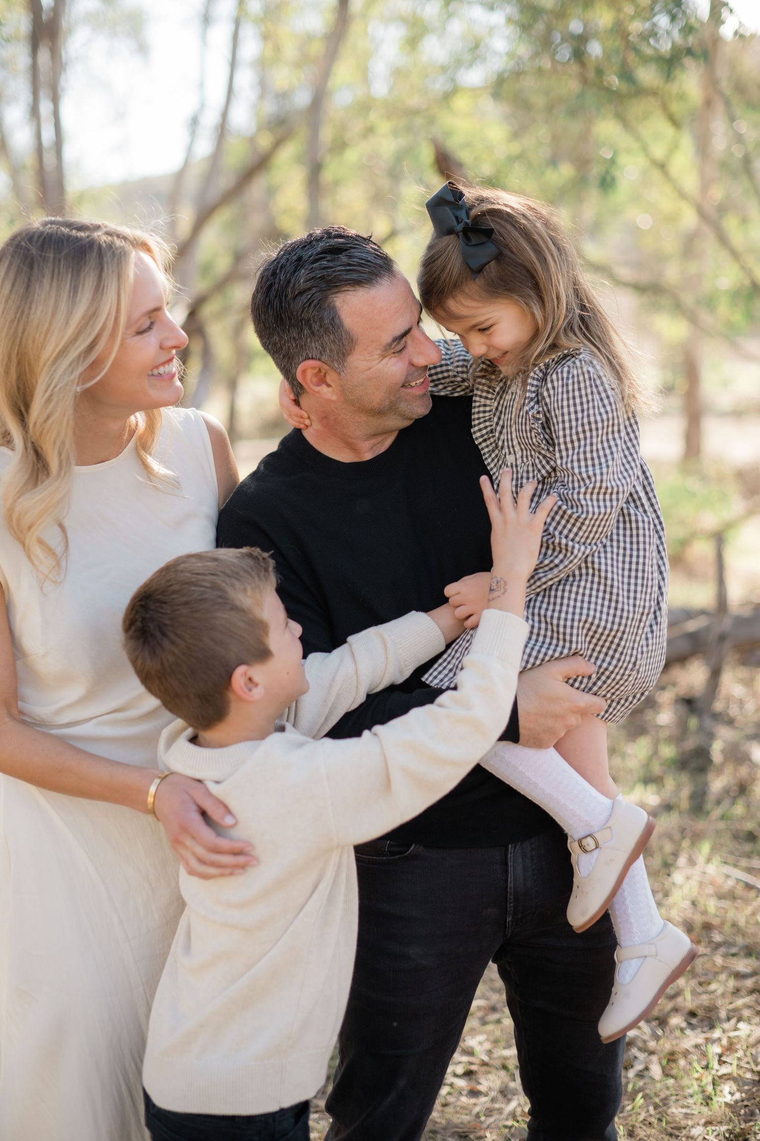 Happy family of four enjoying an outdoor photo session, parents smiling at toddler girl in plaid dress held by dad.
