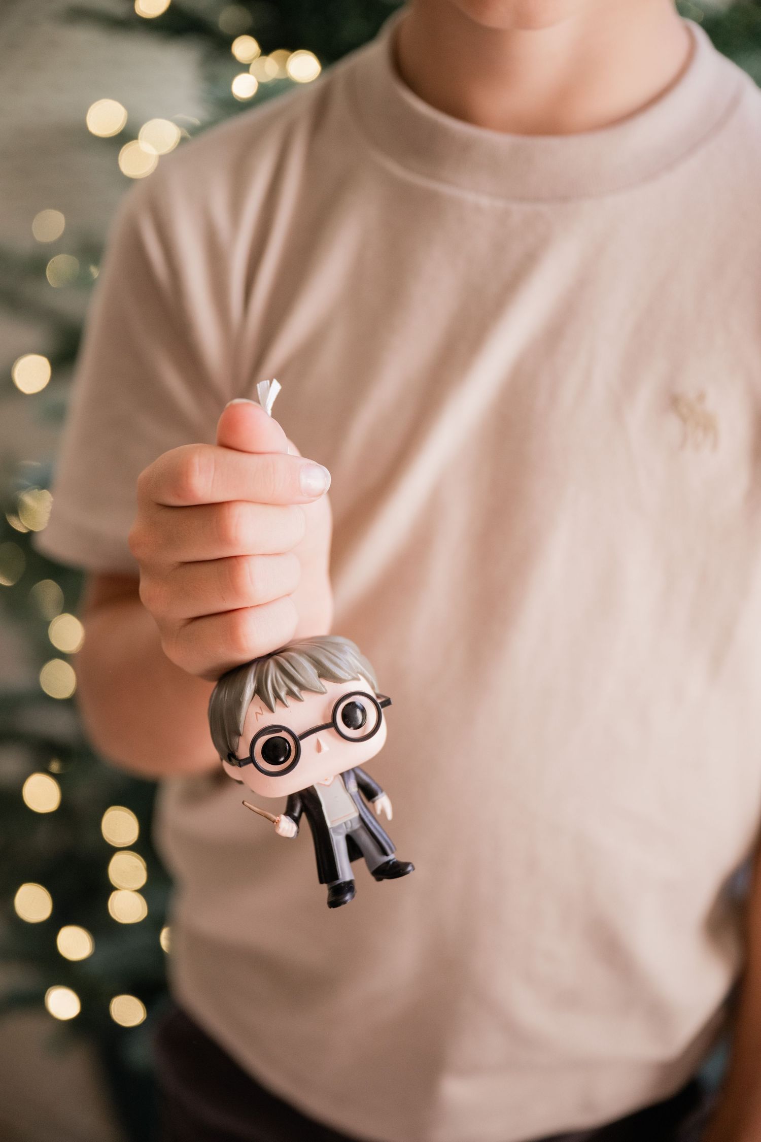 Child holding a Harry Potter Funko Pop figure in front of a Christmas tree with bokeh lights.