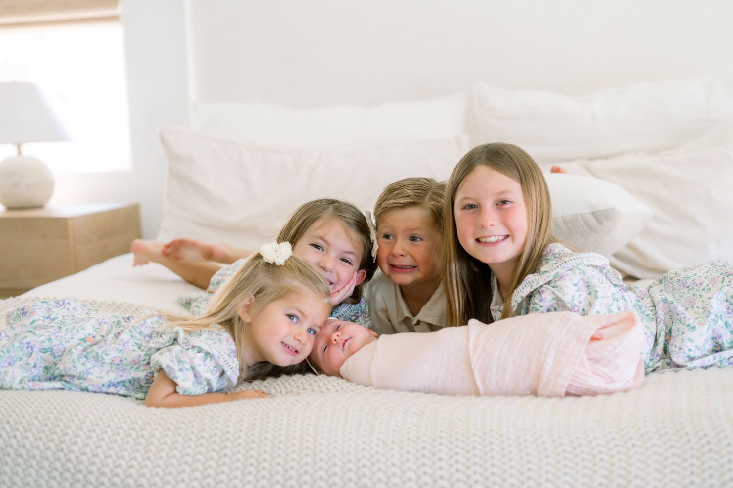 Four young girls in pajamas smiling and lying together on a white bed.
