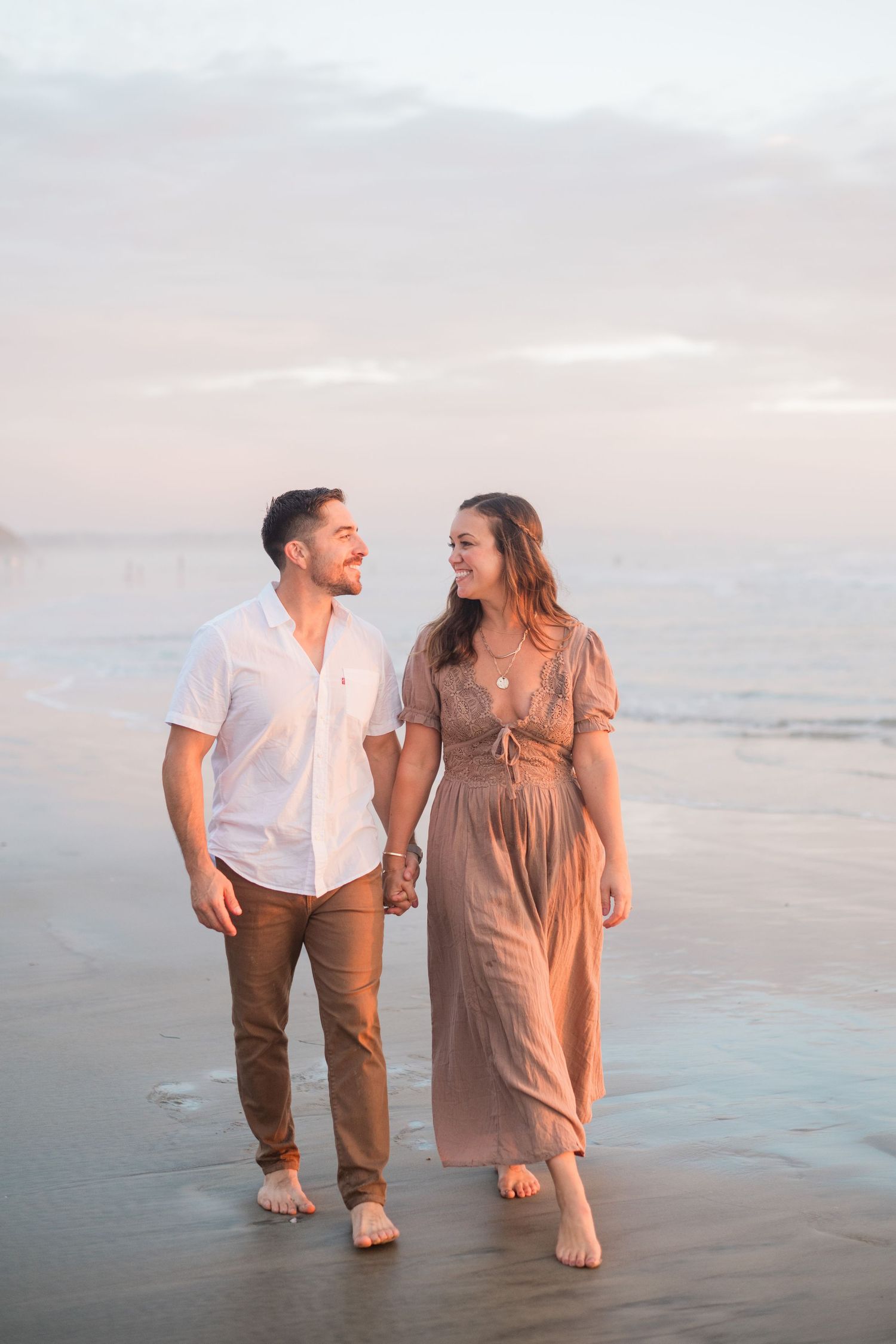A happy couple walks hand-in-hand along a sandy beach at golden hour sunset.