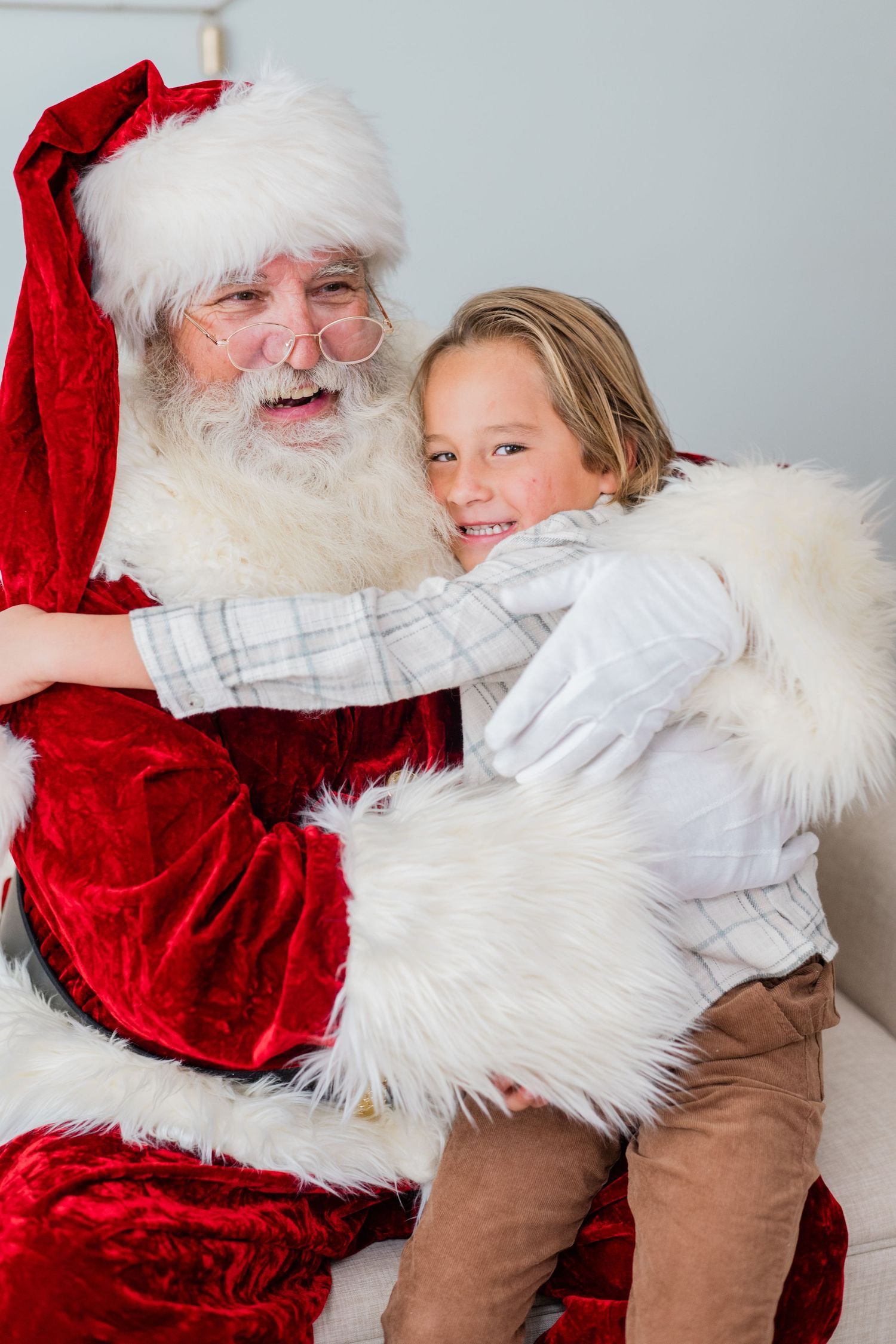 A smiling boy sits on Santa Claus's lap receiving a warm hug during a festive holiday photo session.