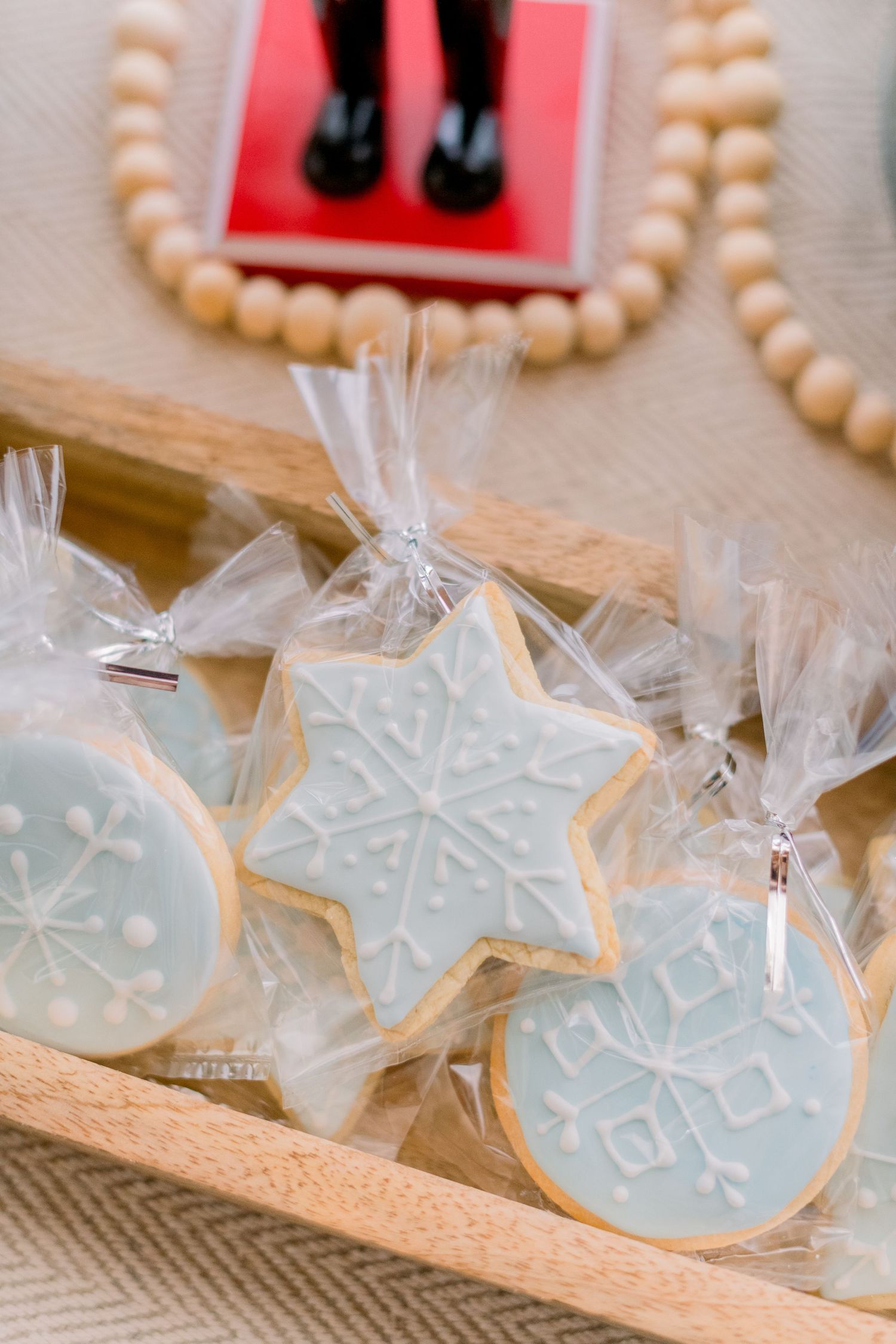 Light blue snowflake-shaped sugar cookies in clear cellophane bags displayed on a wooden tray for a winter holiday party.