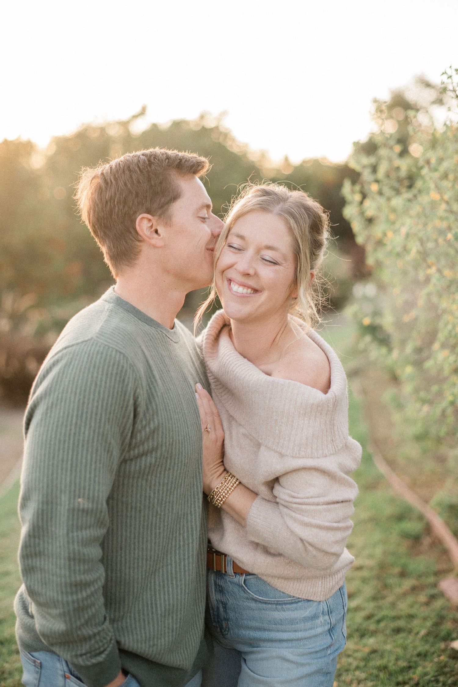 A couple shares a tender moment as the man kisses the smiling woman on the cheek at golden hour.