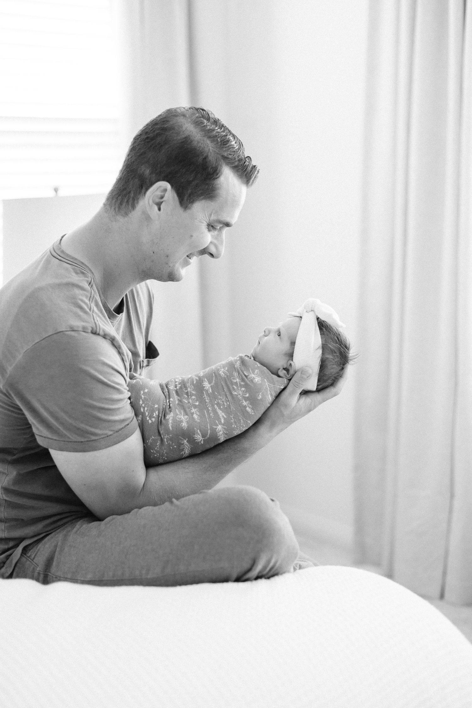 Black and white photo of a father cradling his newborn baby on a bed.